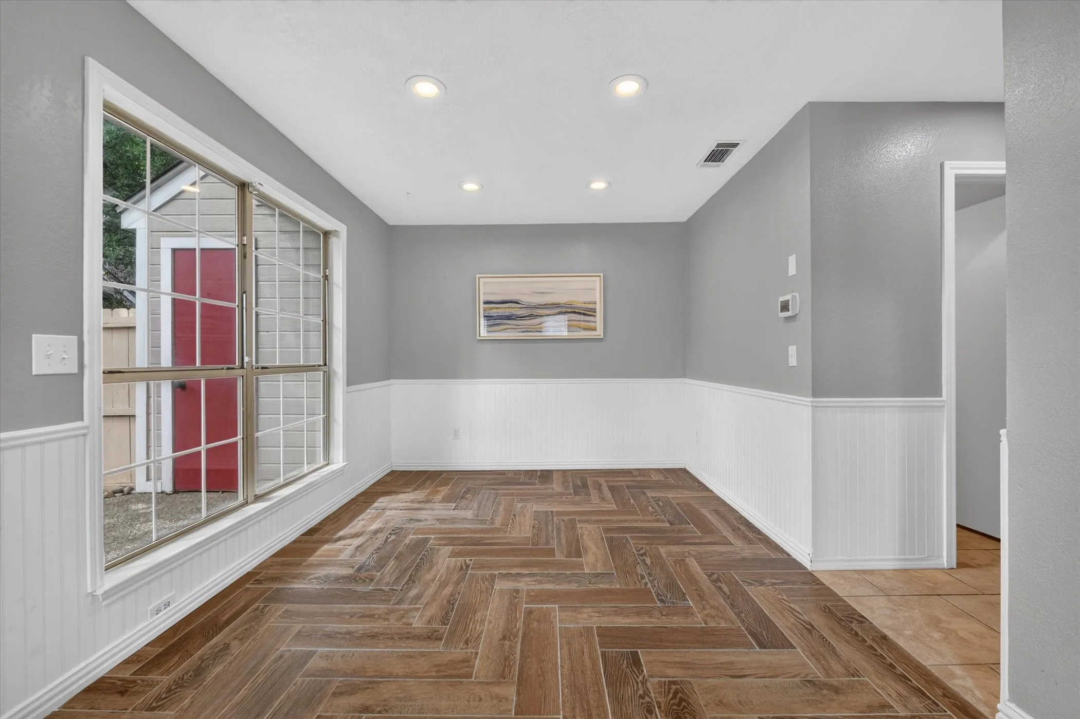 Dining room off the living room has recessed lighting & wainscoting, with windows for natural light.