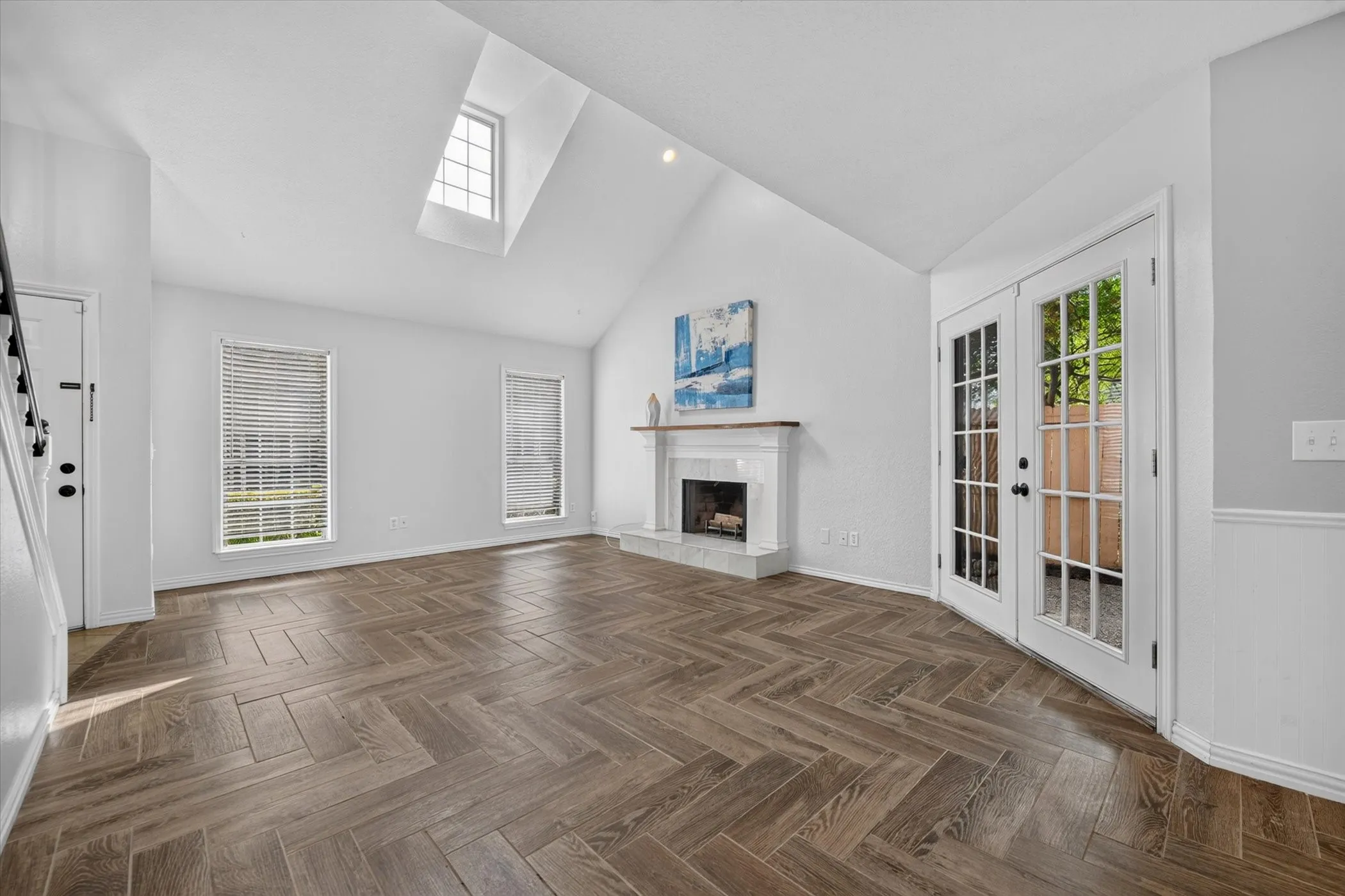 Vaulted ceiling featuring a skylight, wood-look tile flooring in a herringbone pattern, and a fireplace with a wood mantle