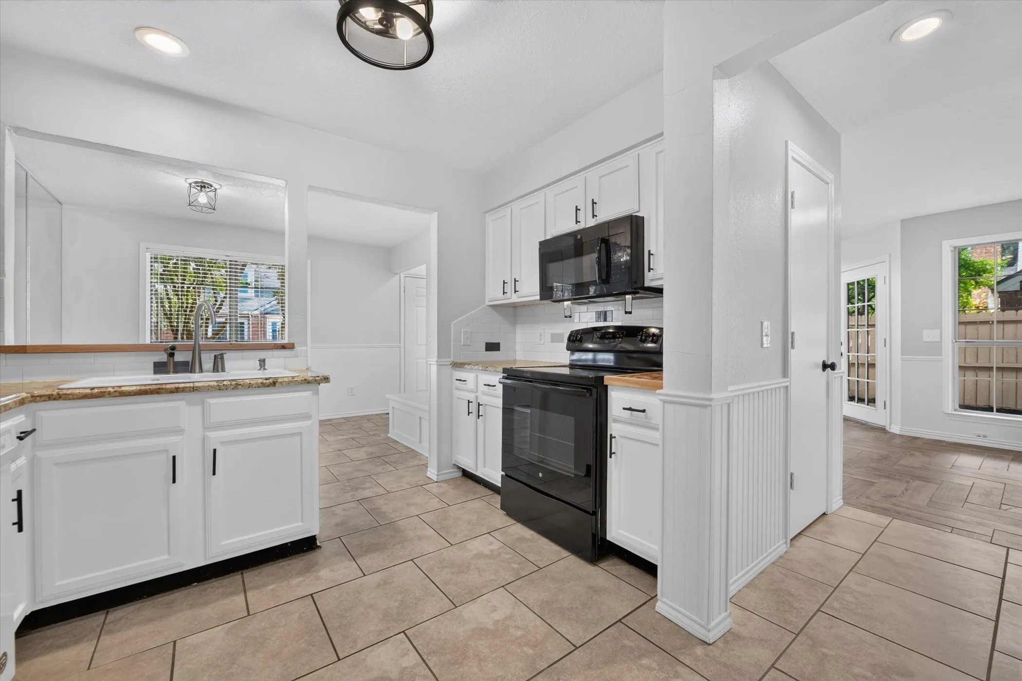 Kitchen featuring white cabinetry, integrated black appliances, a subway tile backsplash, and light-toned tile flooring