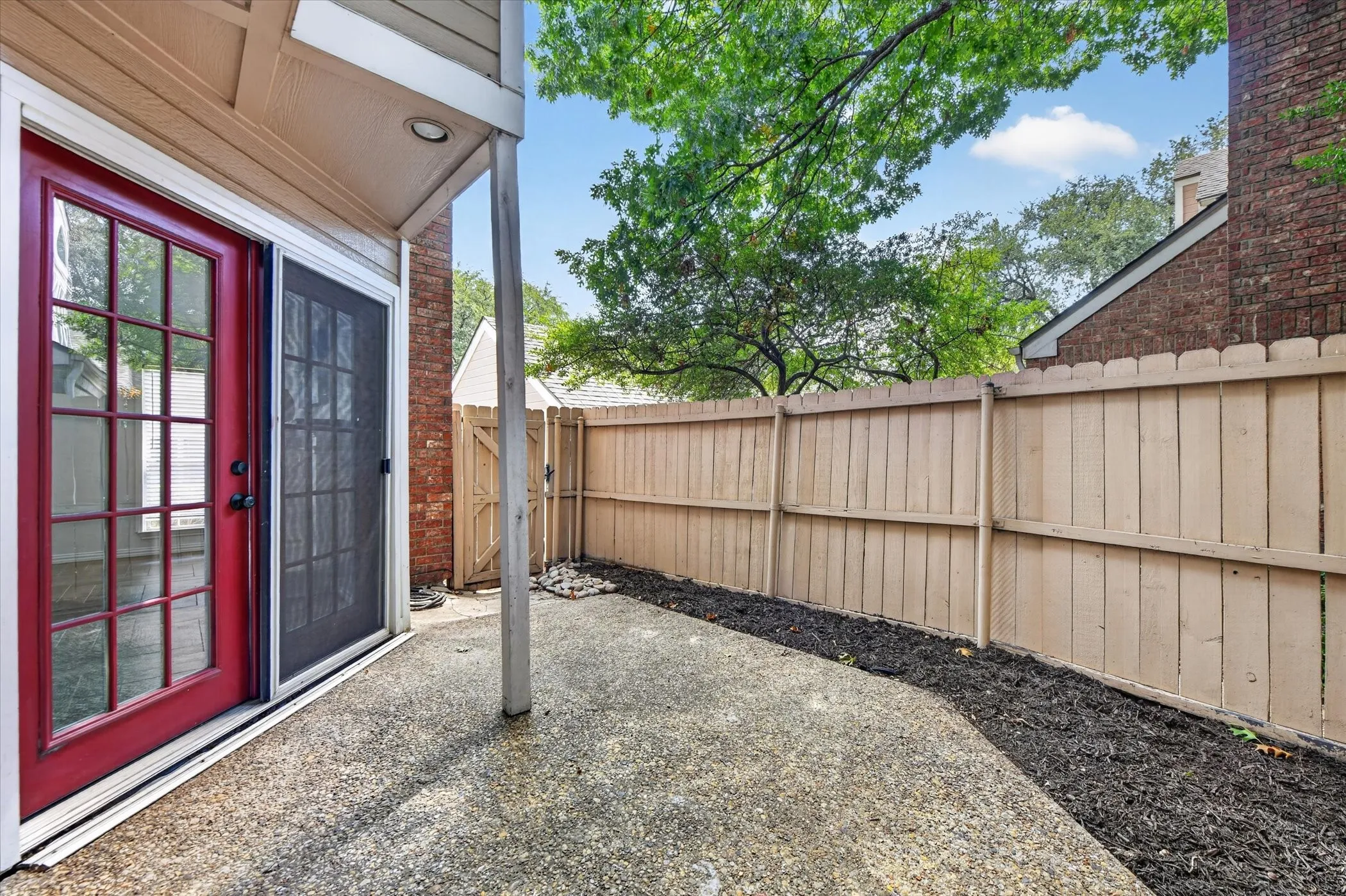 Private patio featuring a red glass-paneled door, sliding screen door, and a full wood fence