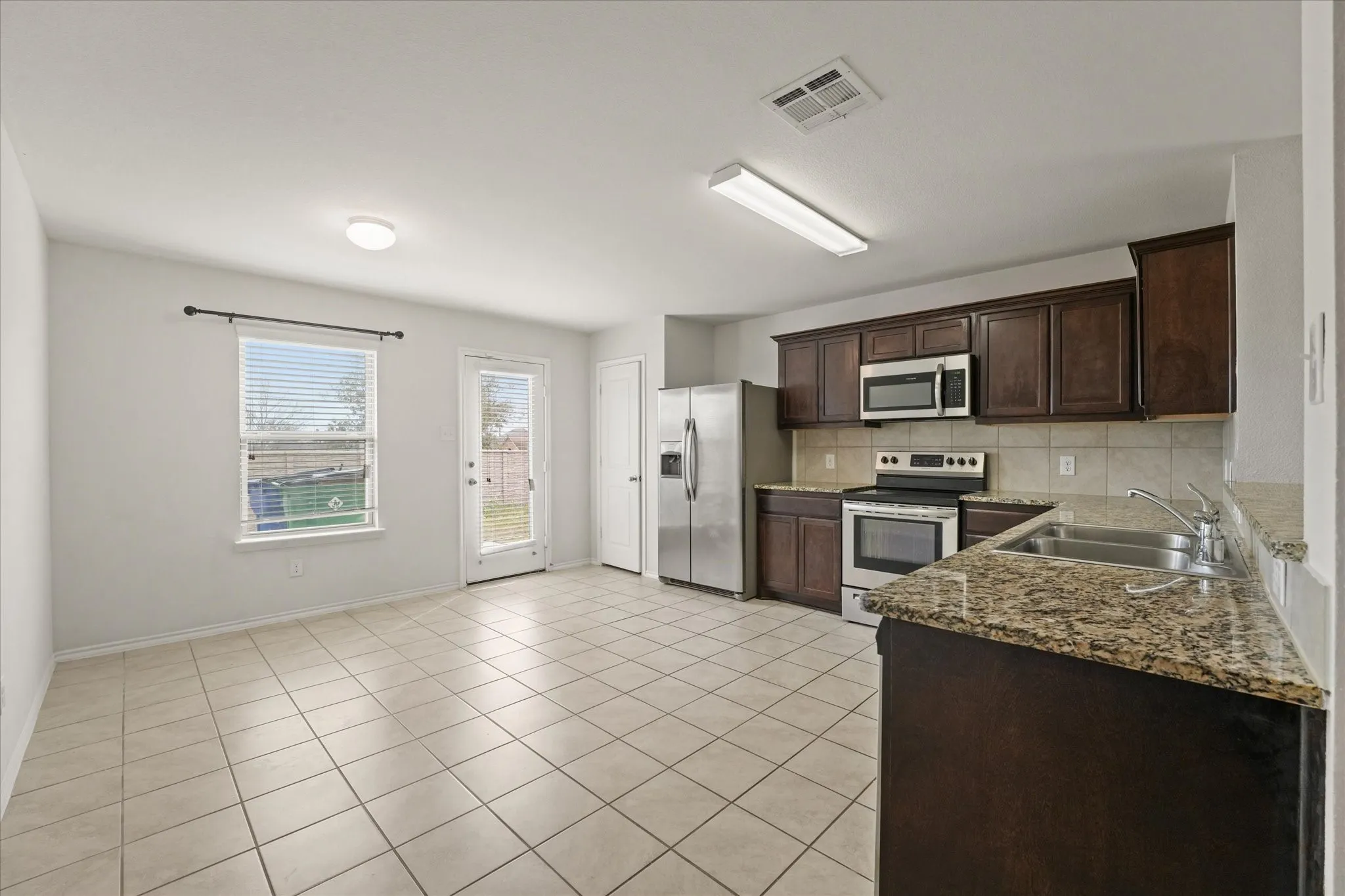 Well-appointed kitchen featuring dark wood-finish cabinetry, stone-finish countertops, stainless steel appliances, and a tile backsplash