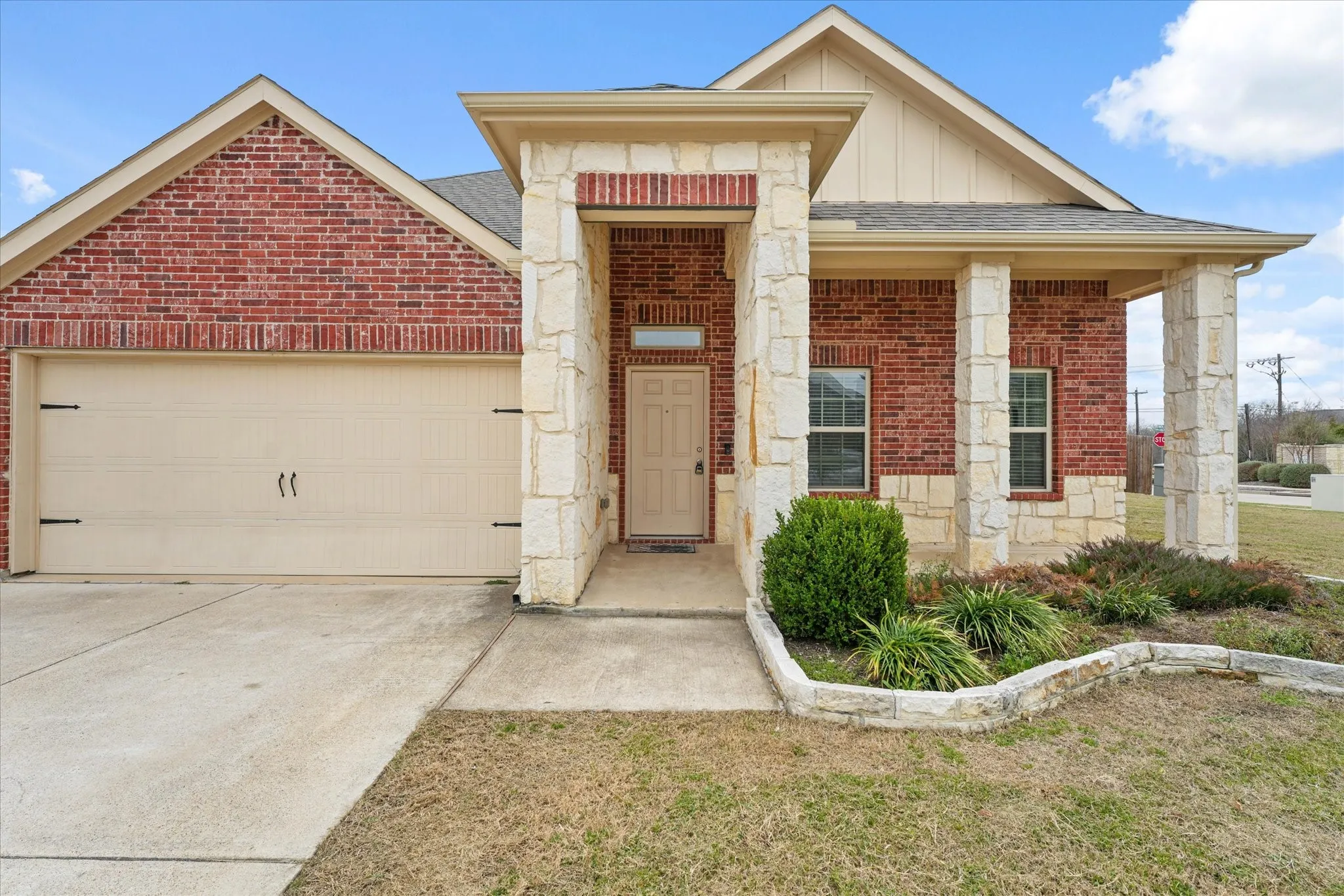 Brick and stone facade with a covered entry, two-car garage, and established landscaping