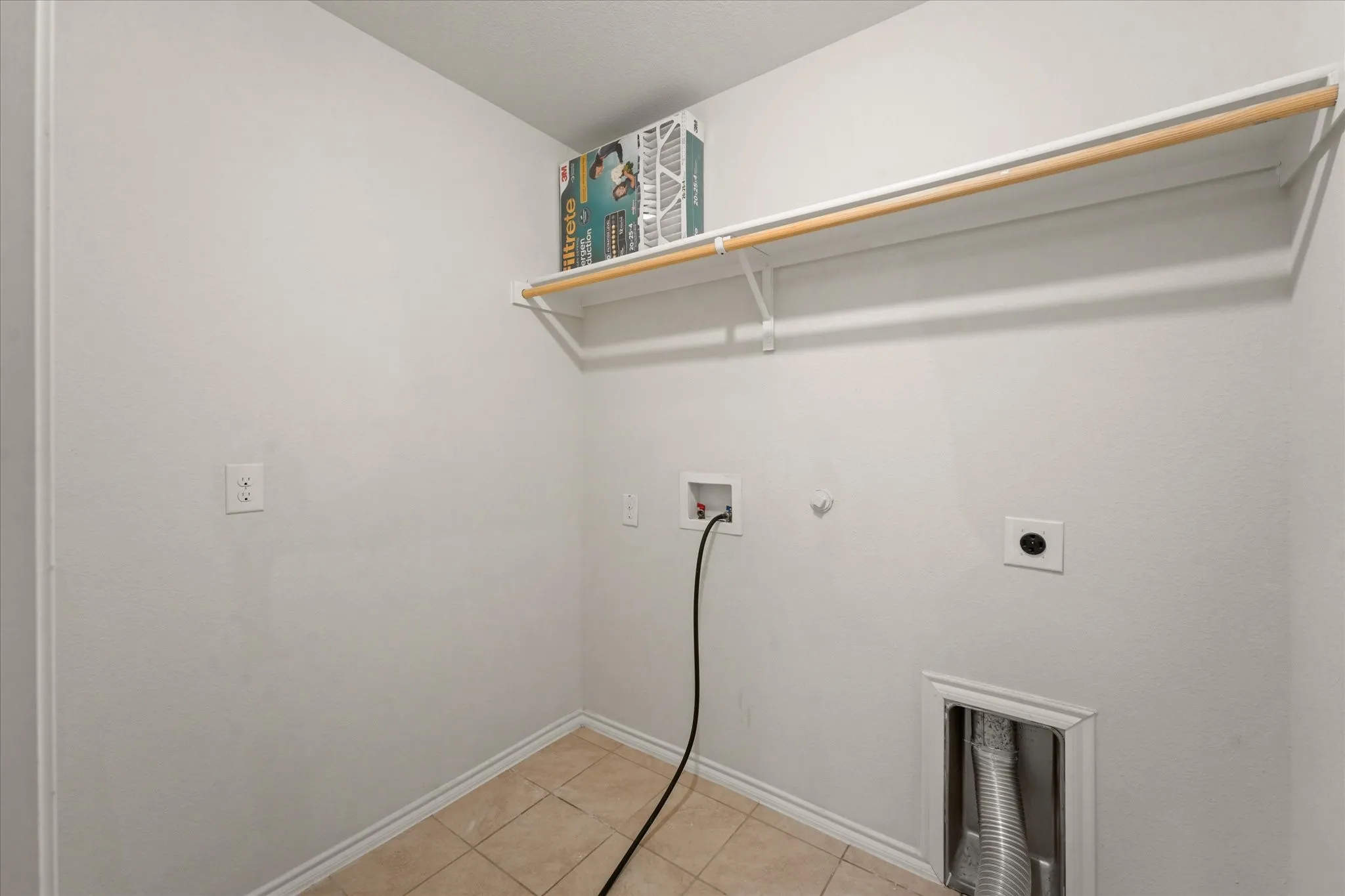 Laundry area with tile flooring and an overhead storage shelf