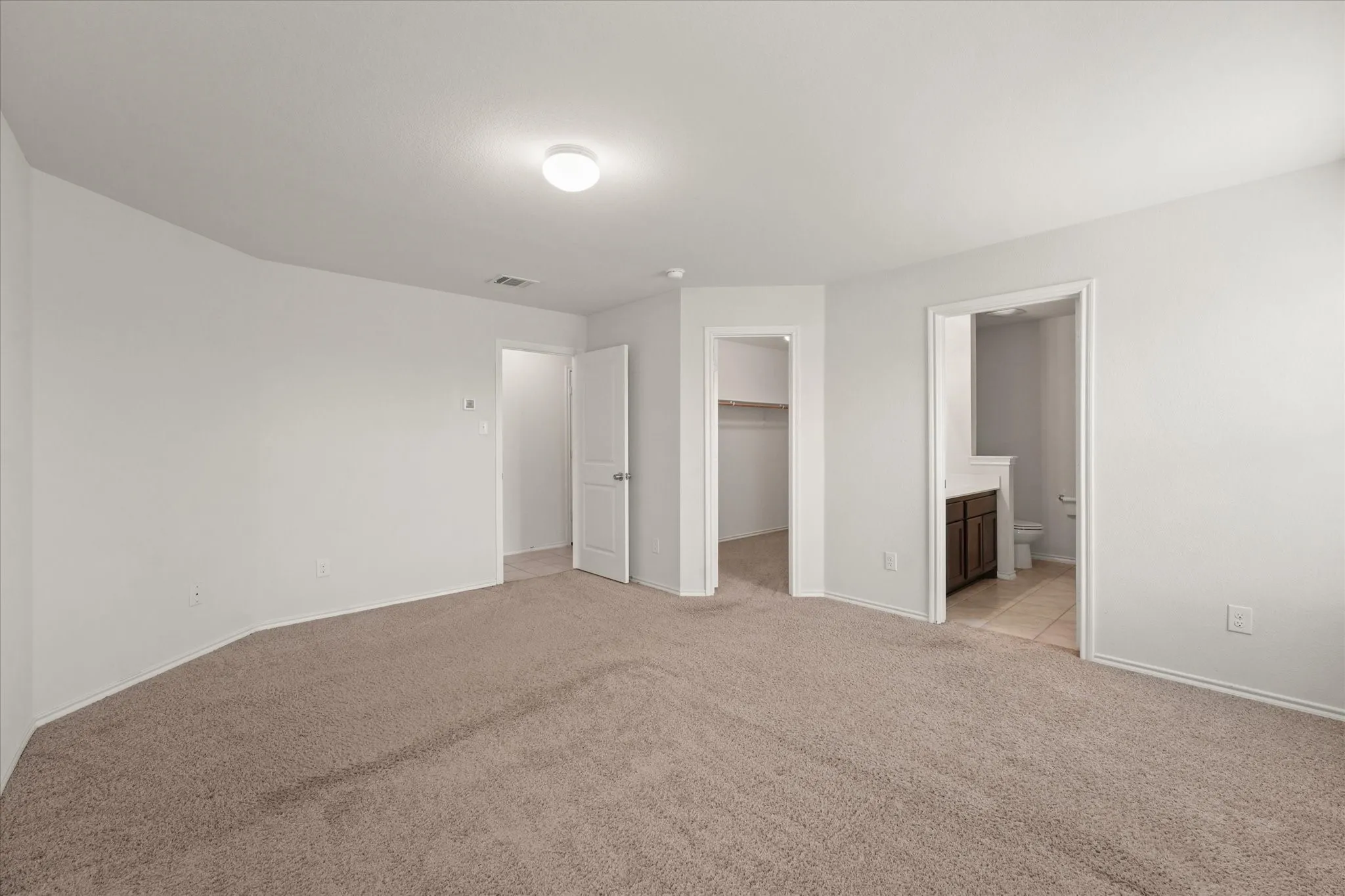 Carpeted room with white walls, ceiling-mounted light fixture, and multiple doorways
