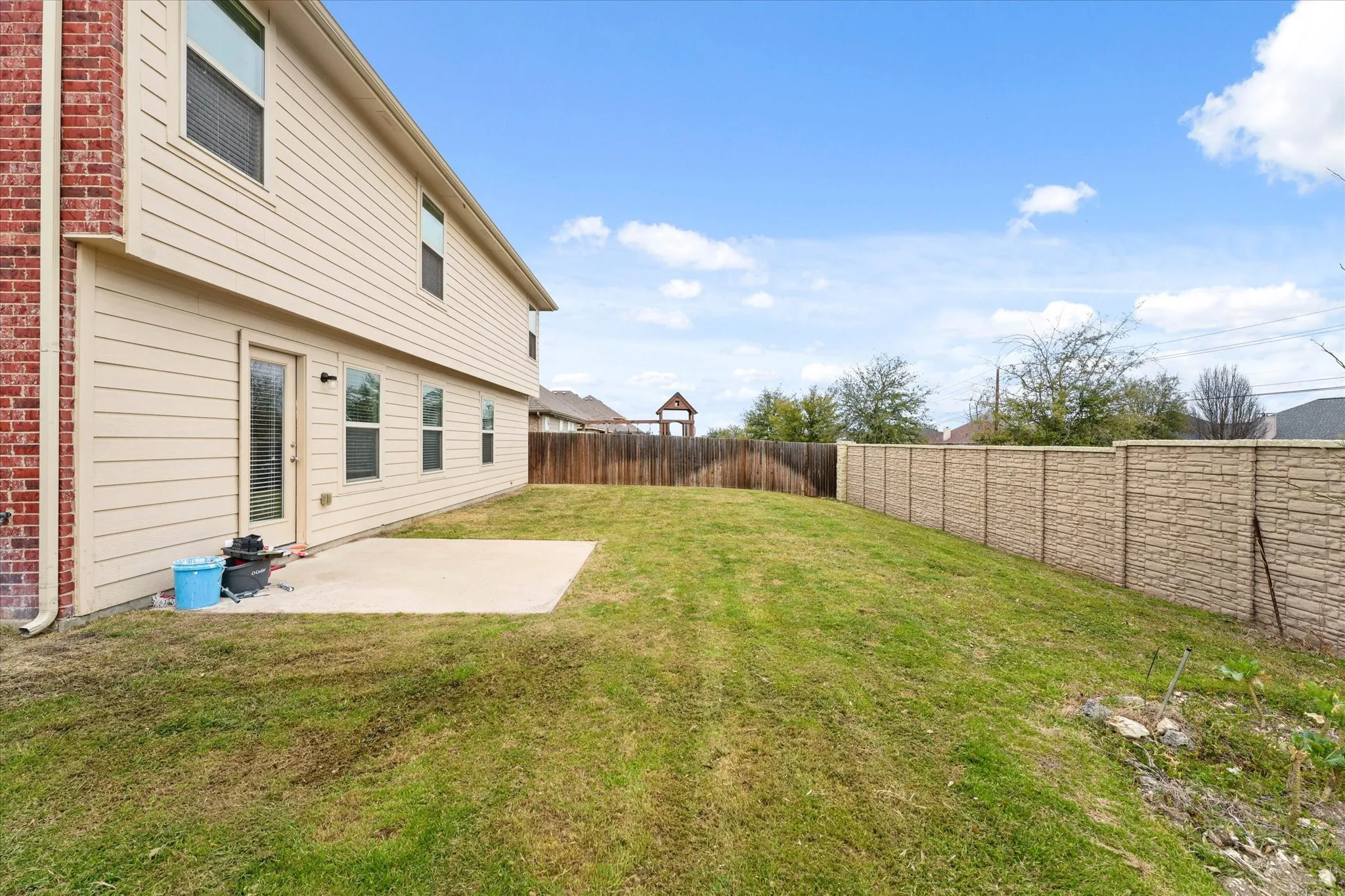 Expansive backyard featuring a concrete patio, a stone-textured privacy wall, and a wooden privacy fence