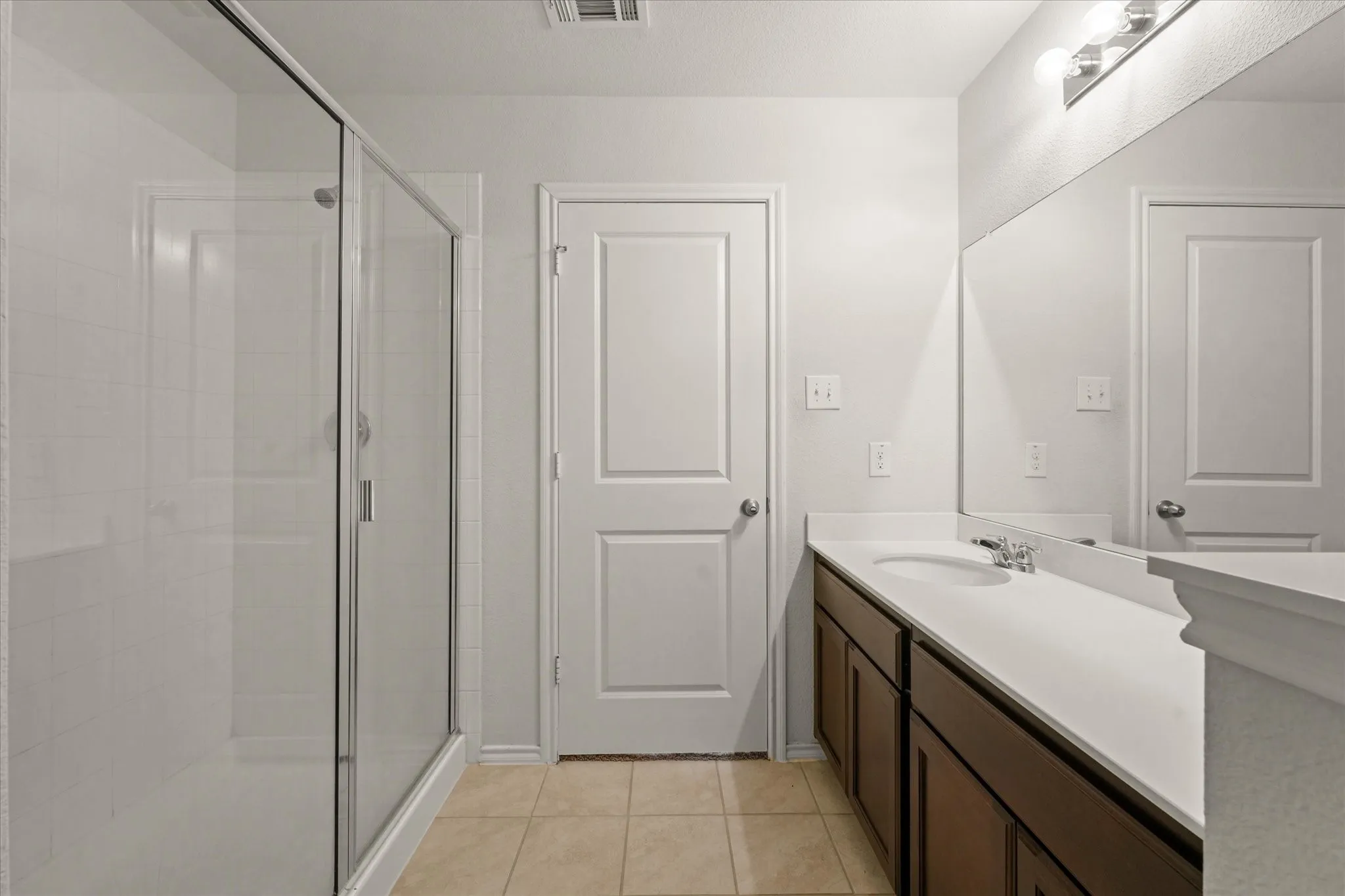 Full-sized mirror, dual under-mount sinks, dark wood-finish vanity, and a glass-enclosed shower