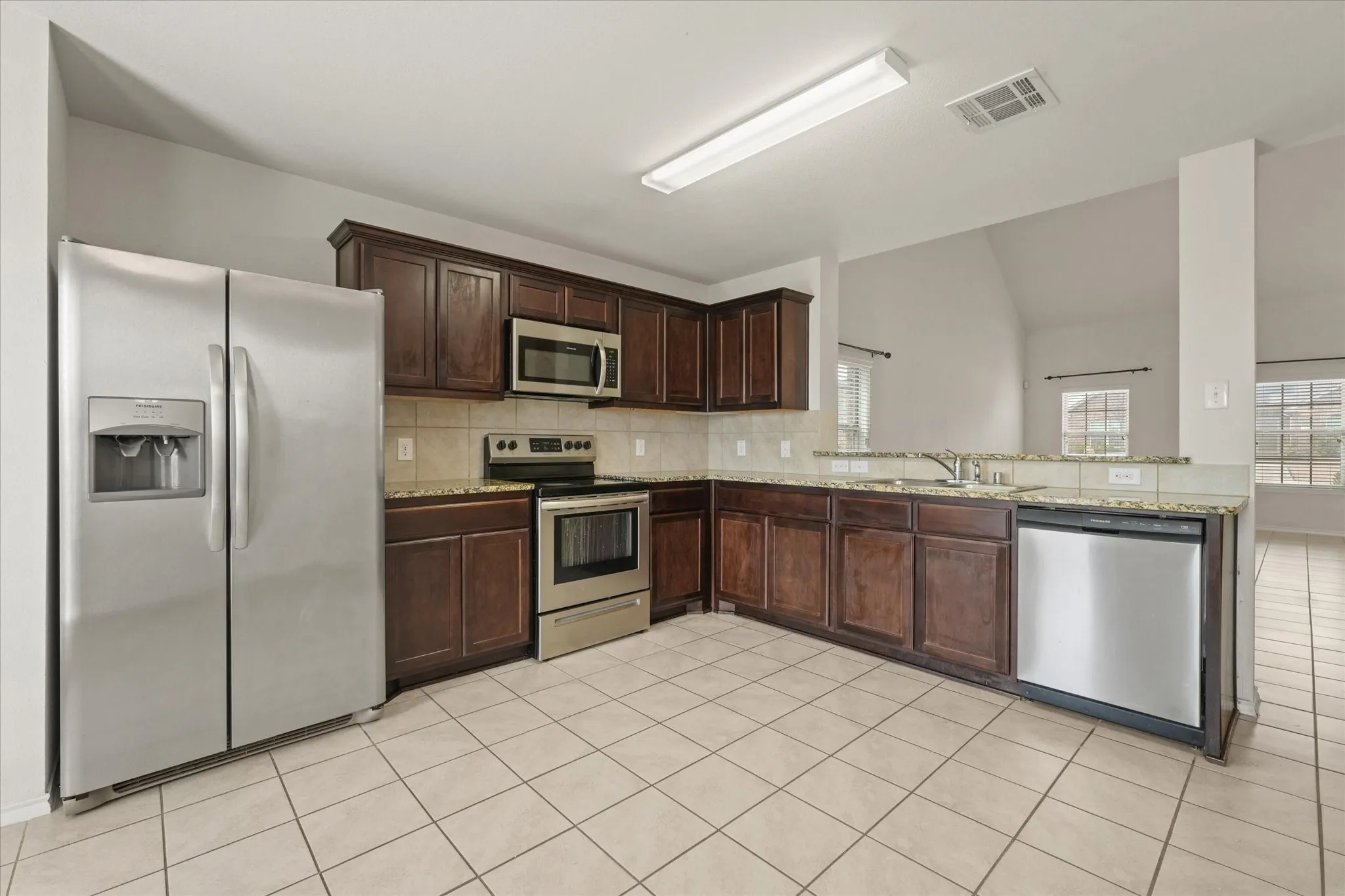 Kitchen featuring stainless steel appliances, dark wood-finish cabinetry, light-toned tile flooring, and speckled countertops