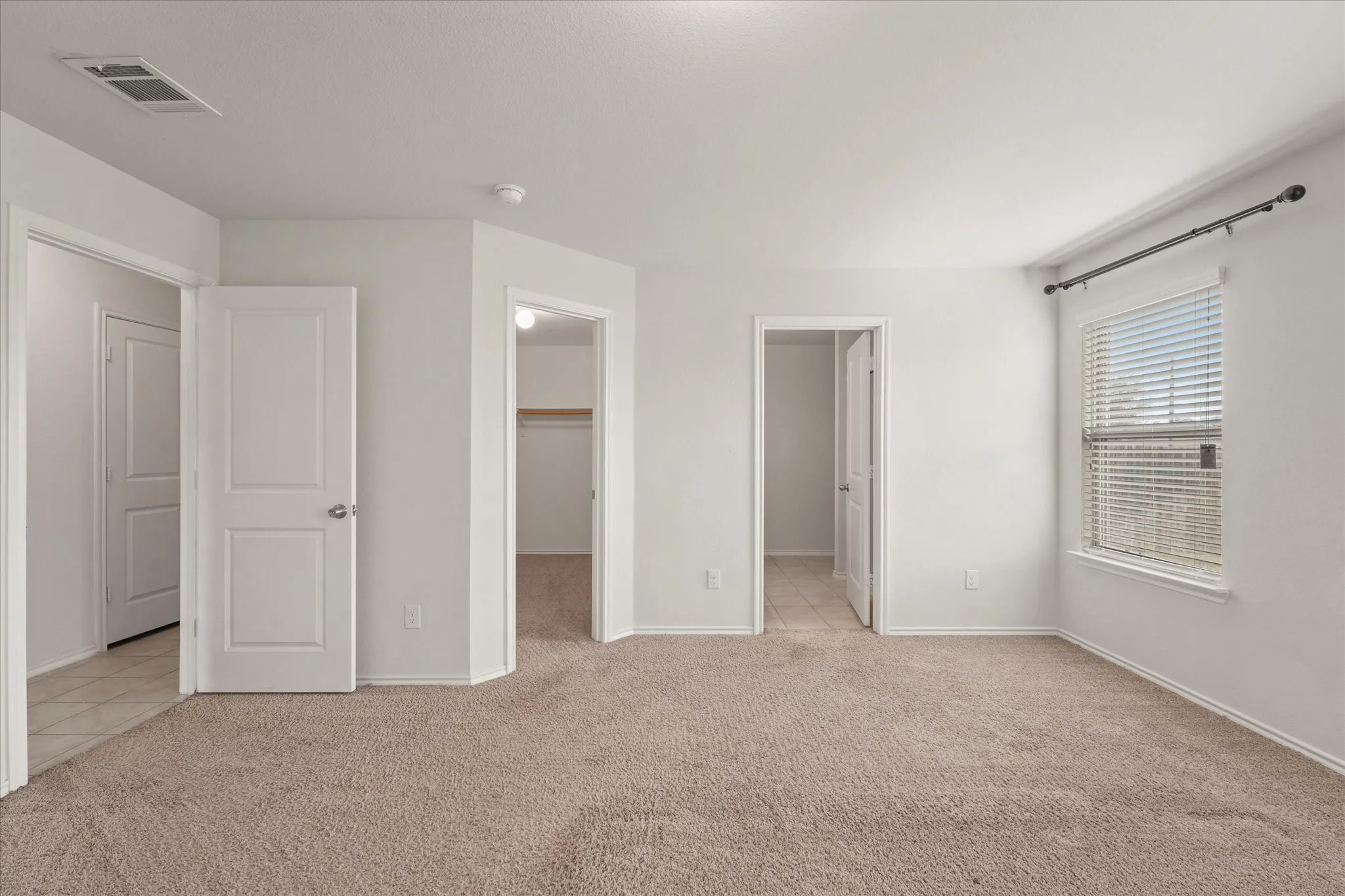 Neutral-toned wall-to-wall carpeting, white interior doors, a window with horizontal blinds, and a built-in closet with shelving