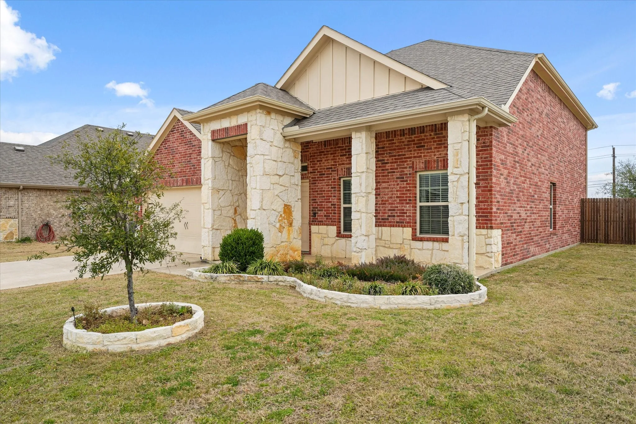 Red brick exterior with stone accents, covered front entry, and a landscaped front yard with stone-edged garden beds