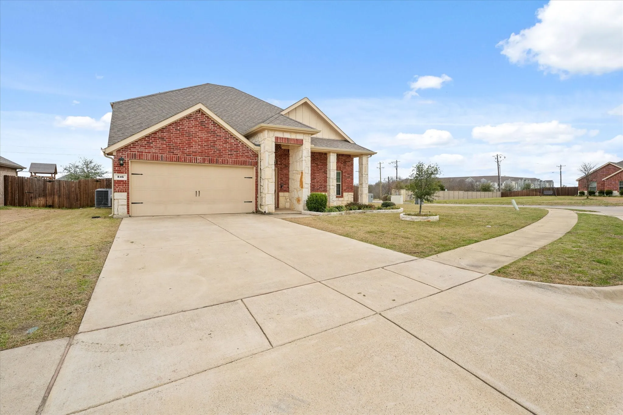 Brick and stone exterior with a two-car garage, concrete driveway, and front yard landscaping