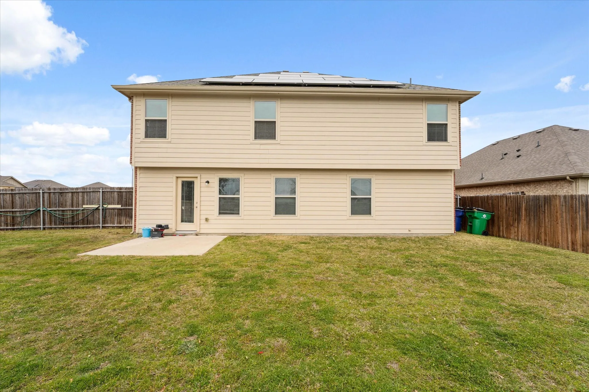 Two-story structure with horizontal siding, multiple windows, and a ground-level patio