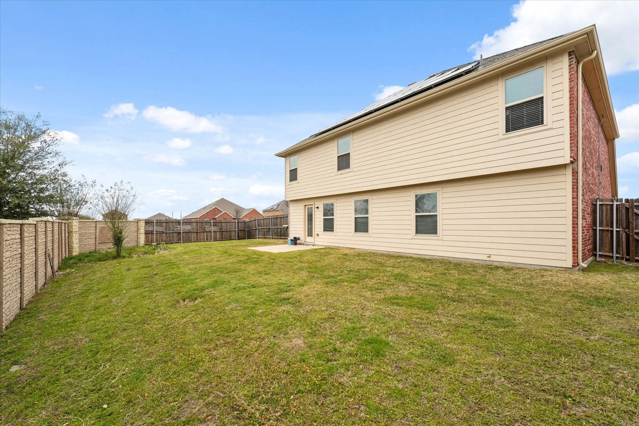 Expansive green space featuring a concrete patio, a privacy fence, and a two-story exterior with siding and brick accents