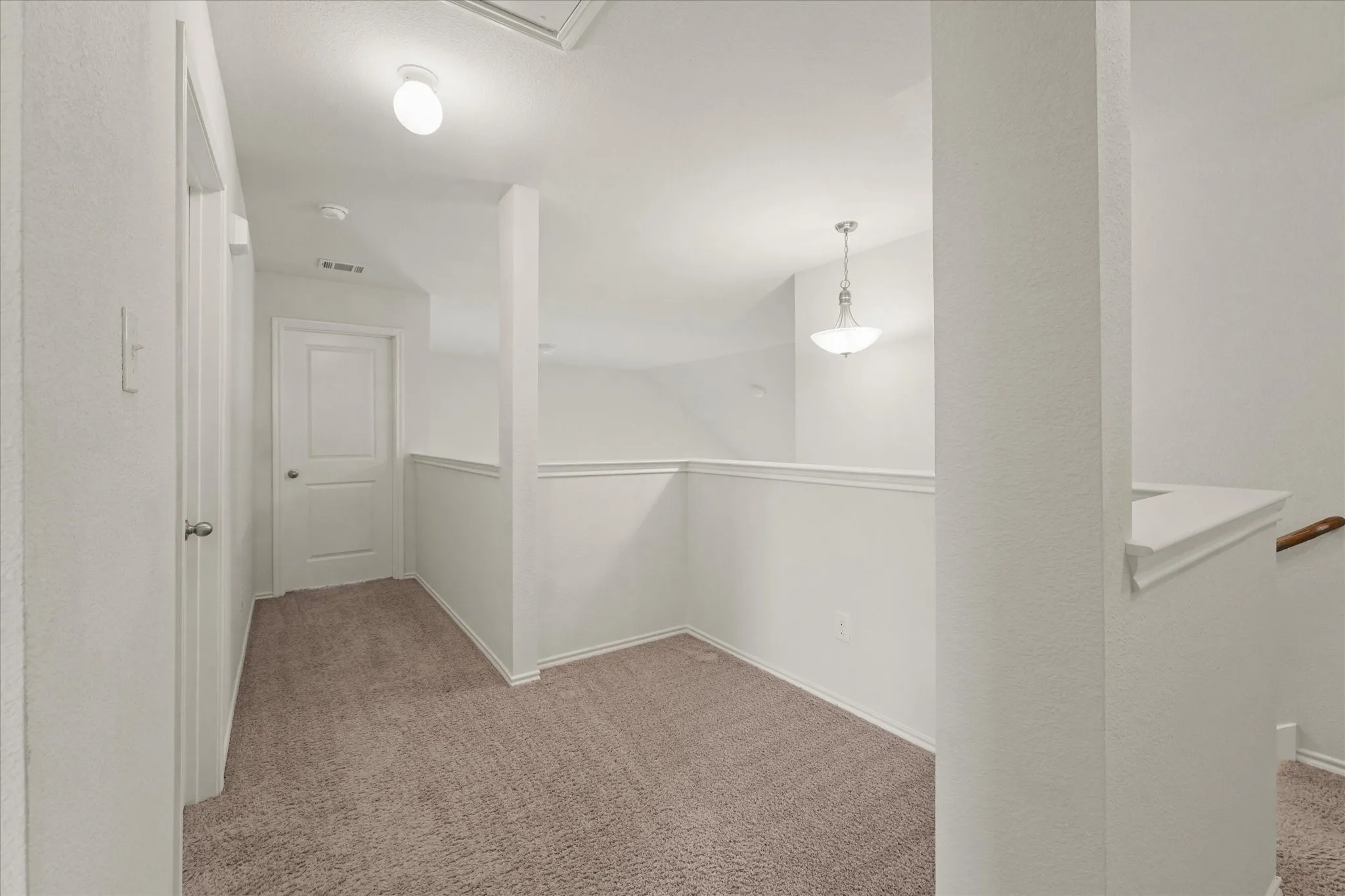 Carpeted loft area featuring a pendant light fixture and white painted railings
