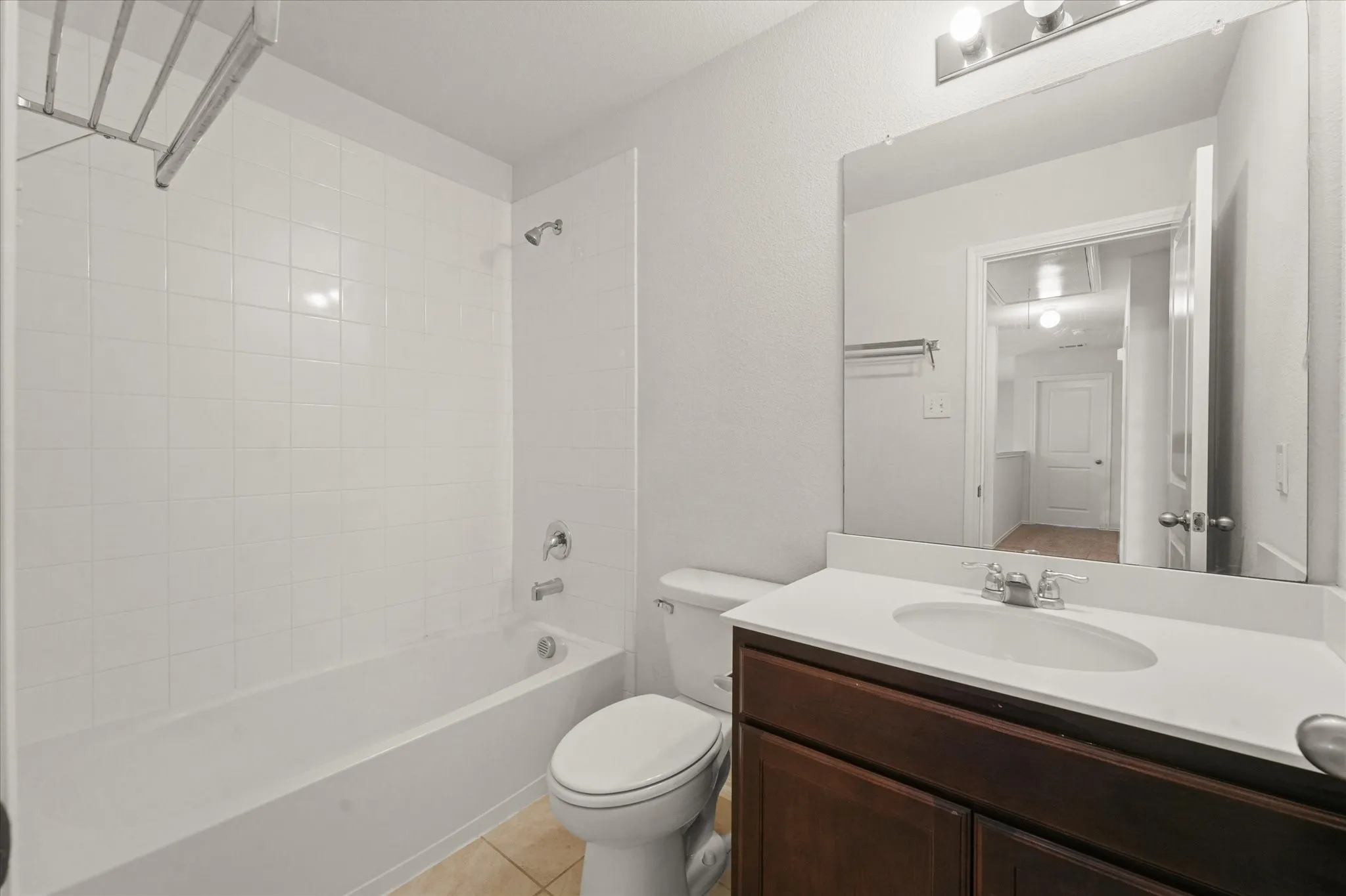 Bathroom featuring a vanity with an integrated sink, wood-finish cabinetry, a framed mirror, and a tiled tub with shower