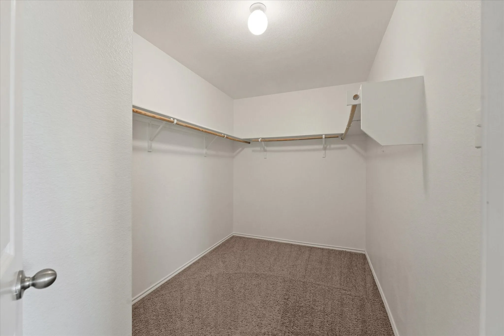 Wall-to-wall carpeting with built-in shelving, hanging rods, and an overhead light fixture
