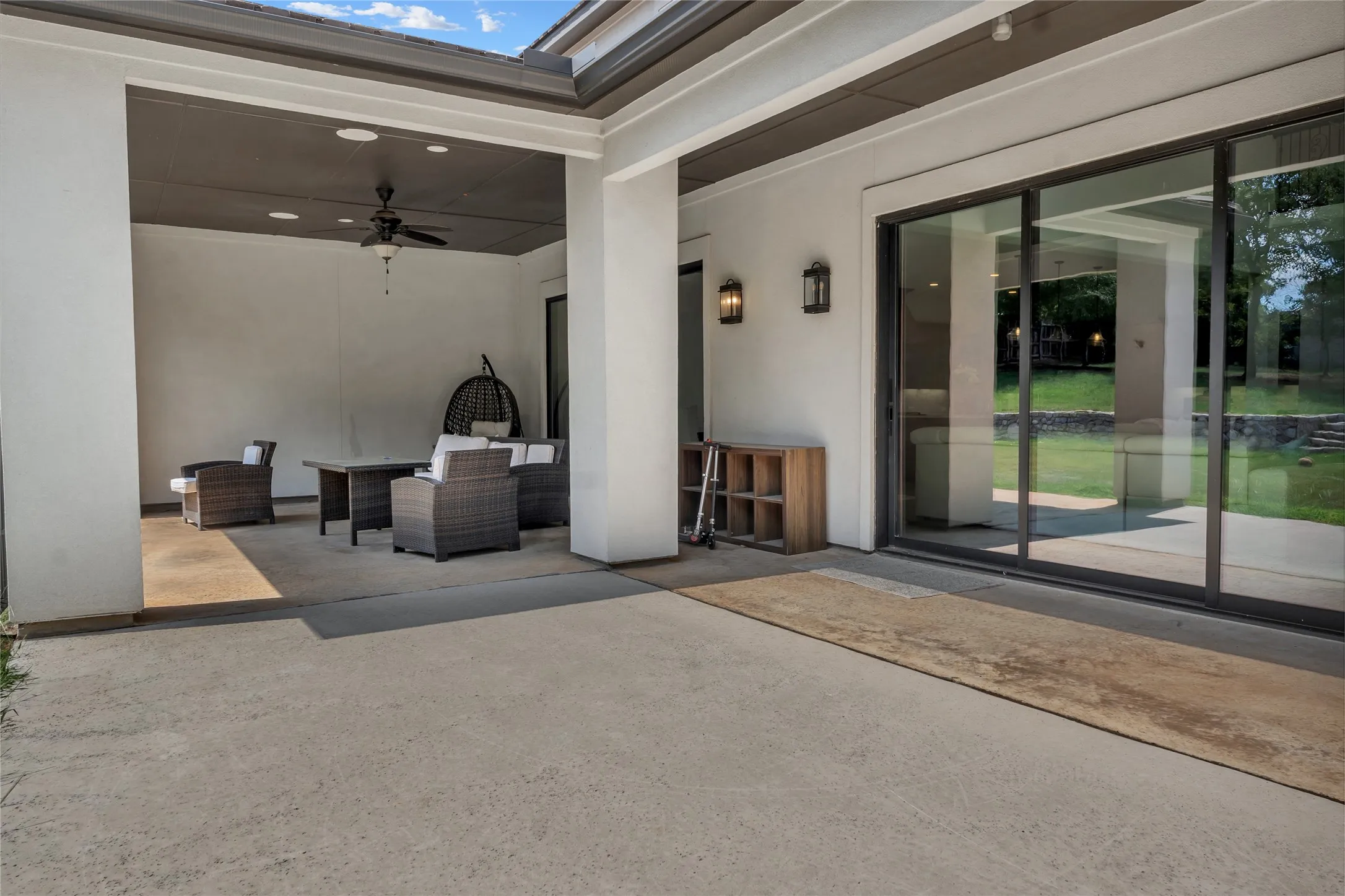 Expansive outdoor patio featuring a covered seating area with a ceiling fan, recessed lighting, and dual wall sconces