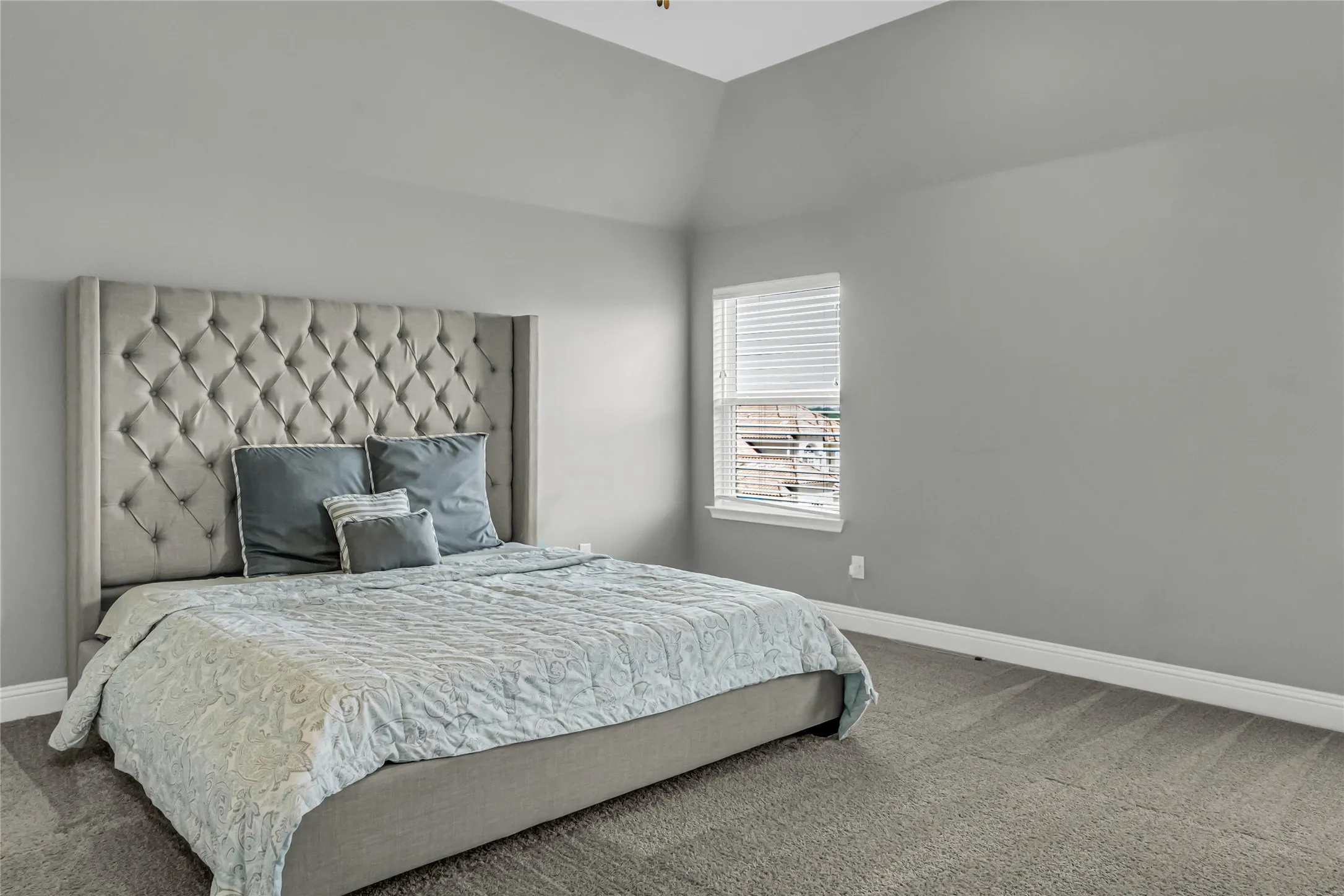 Vaulted ceiling, neutral wall paint, carpeted flooring, window with blinds, and white trim