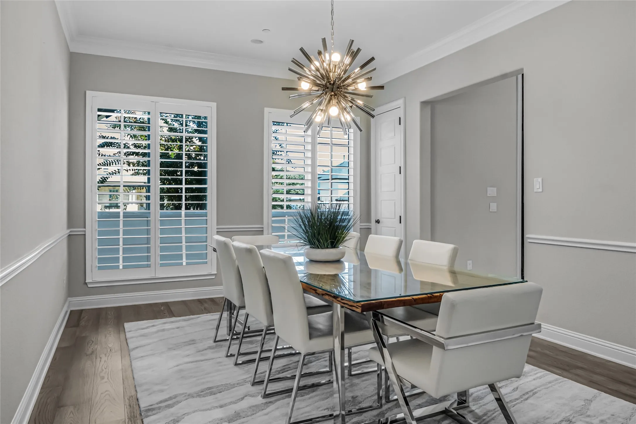 Dining area featuring wood-finish flooring, white plantation shutters, crown molding, and wainscoting