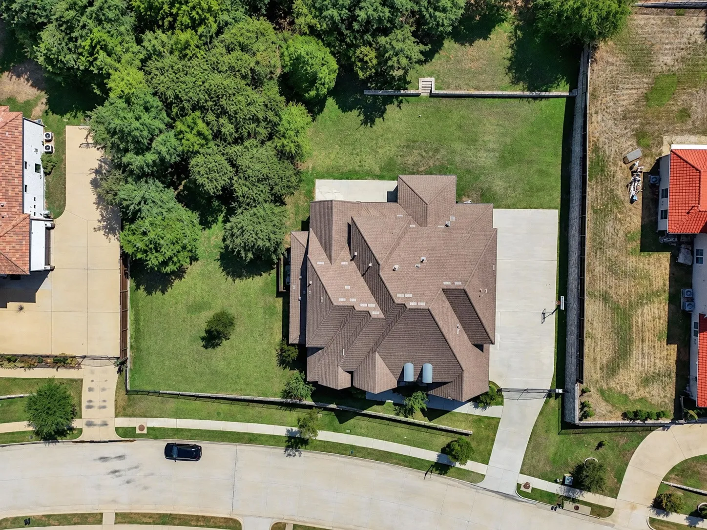 Manicured lawn, mature trees, concrete driveway, paved street, and neighboring properties