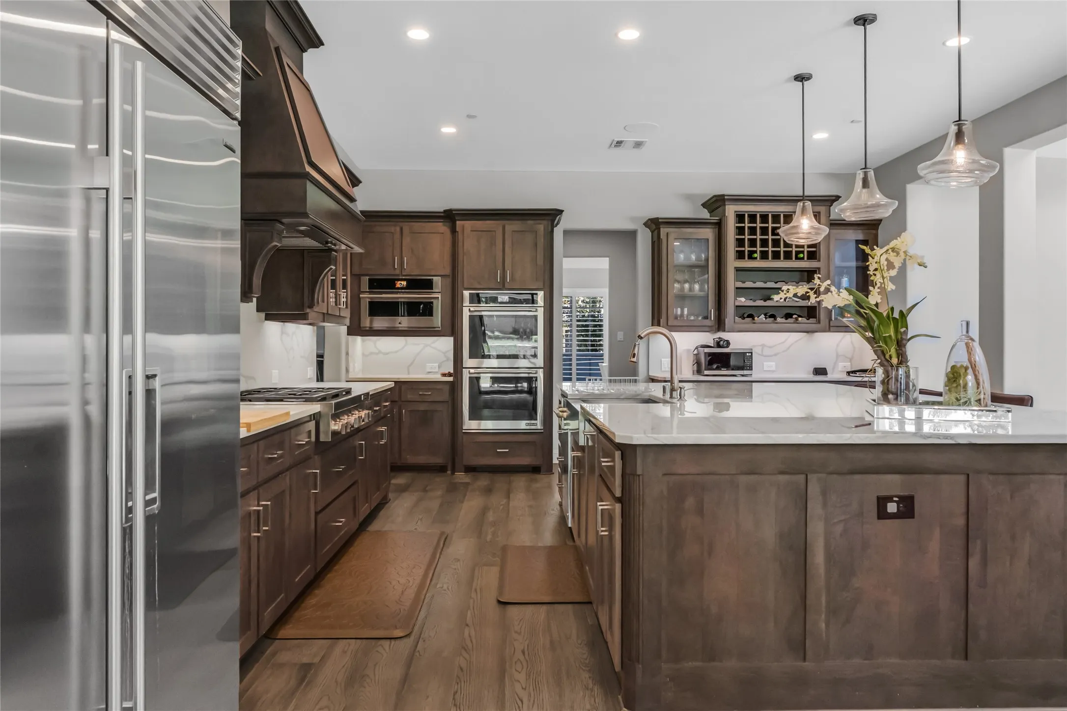 Gourmet kitchen featuring stainless steel appliances, a built-in wine rack, quartz countertops, wood-finish flooring, and pendant lighting