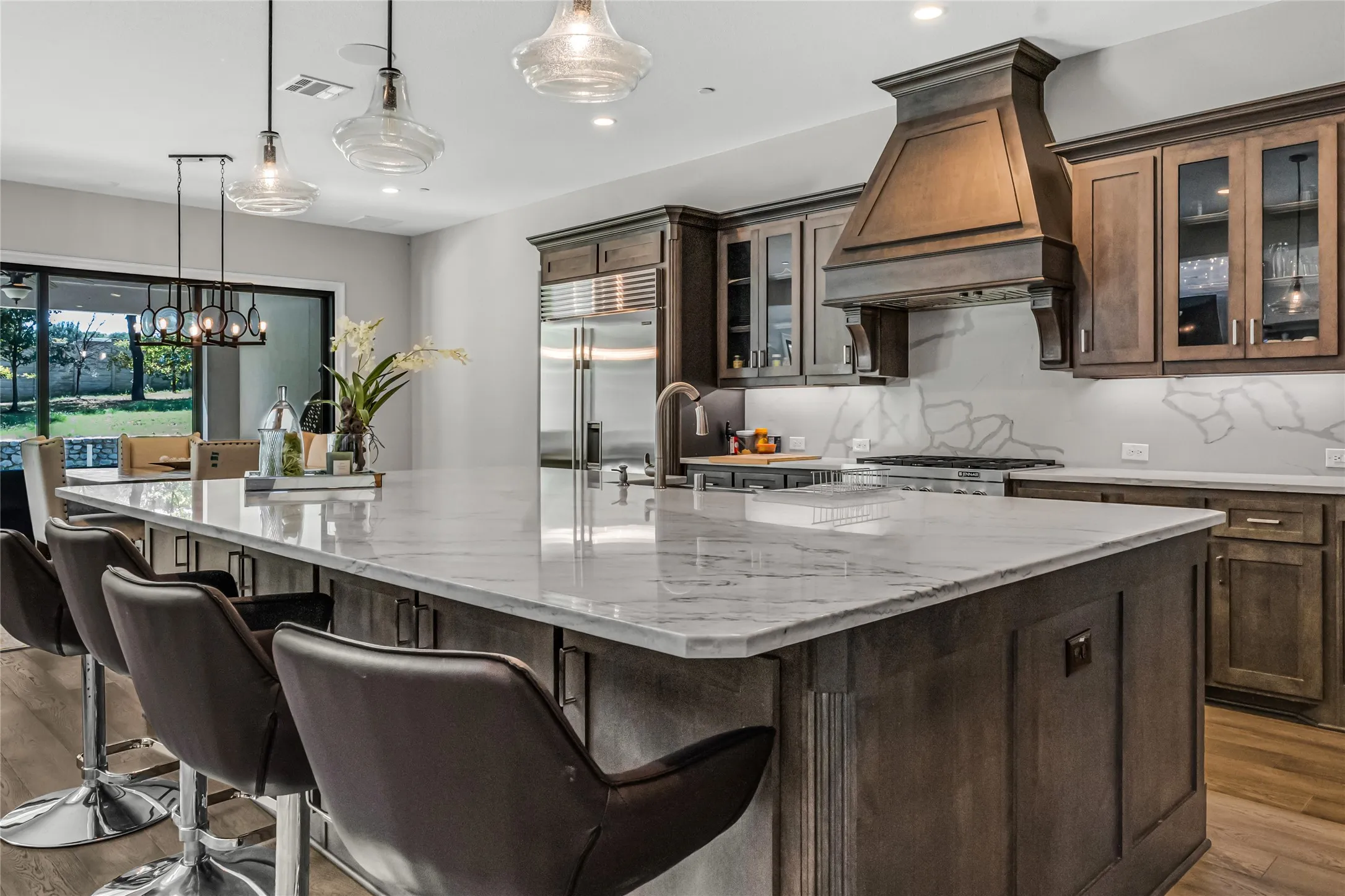 Spacious kitchen island with a light-toned countertop, dark wood-finish cabinetry, stainless steel appliances, and a matching wood-finish range hood