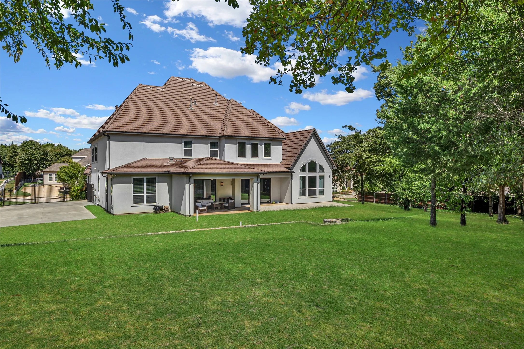Stucco exterior with a tiled roof, expansive lawn, covered patio, and large arched window