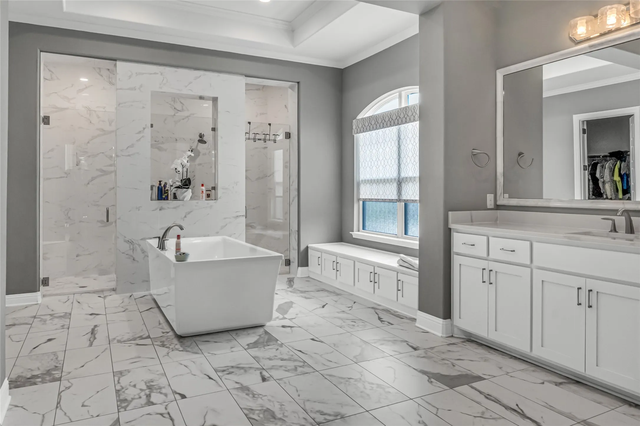 Freestanding tub, glass-enclosed shower, dual vanity with undermount sinks, built-in window bench with storage, and large format tiled flooring