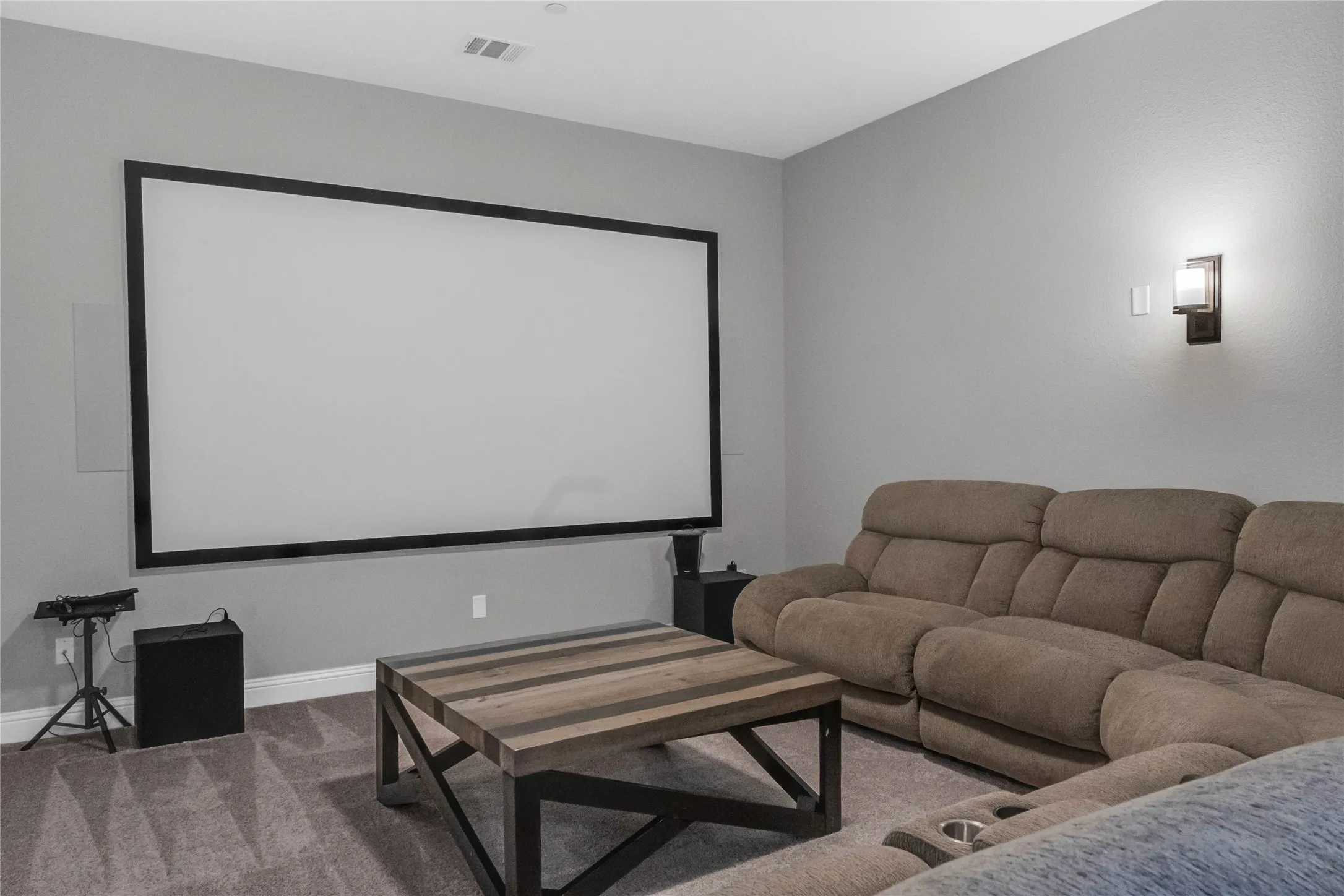 Large projection screen, recessed ceiling lighting, wall-mounted sconce, and neutral wall color