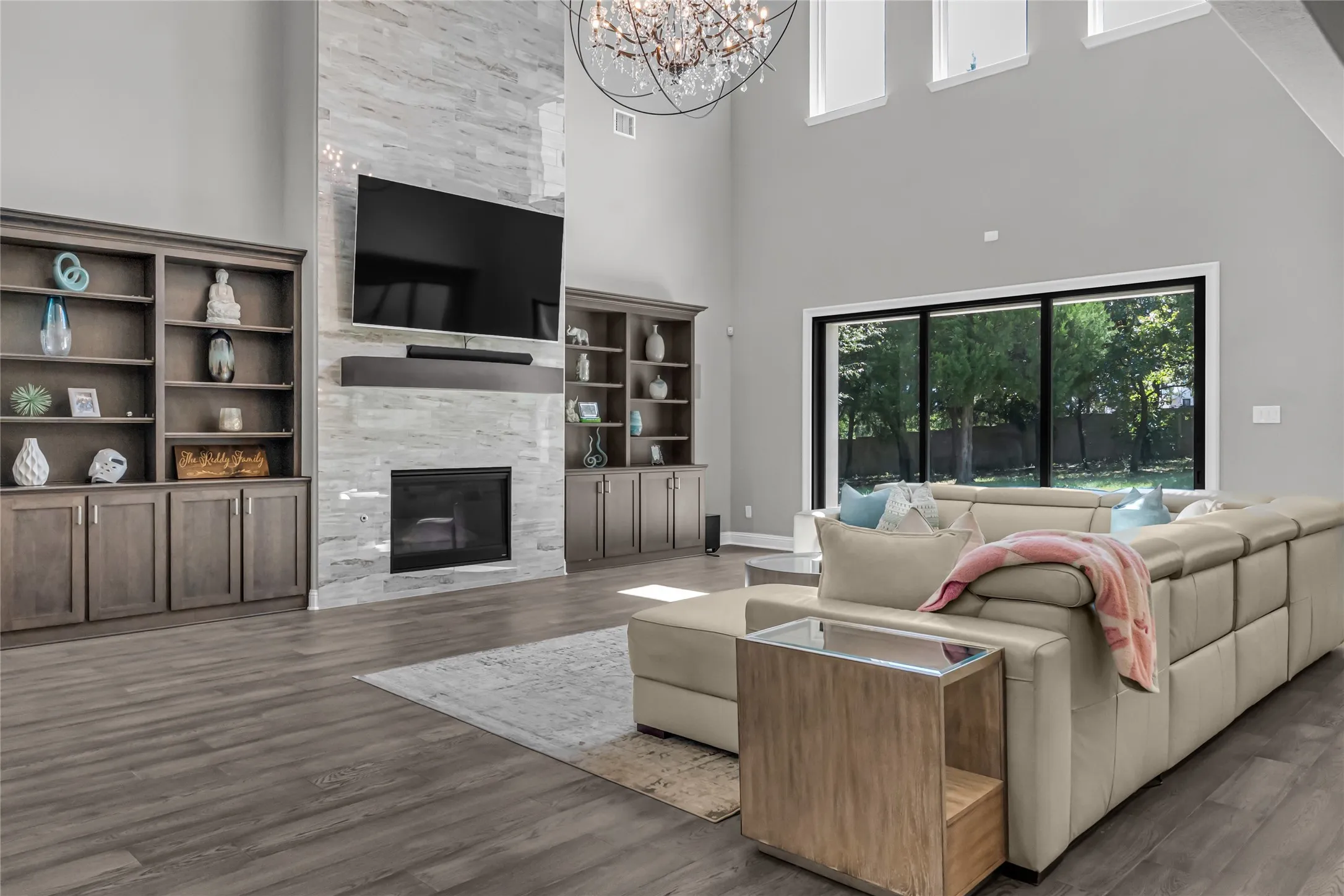 Vaulted ceiling with a chandelier, floor-to-ceiling stone-look fireplace, built-in shelving with cabinetry, wood-finish flooring, and large picture windows