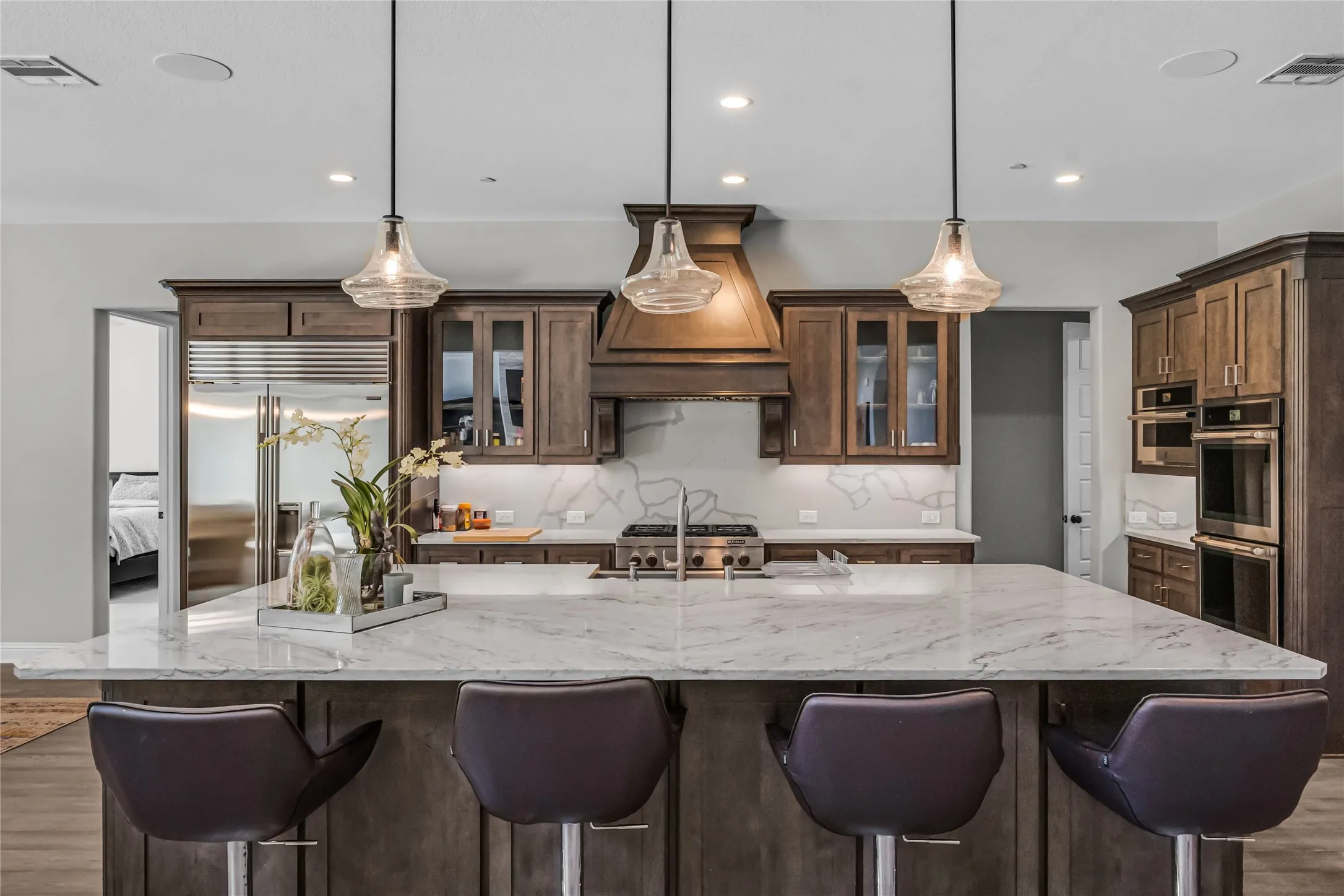 Spacious kitchen with a large central island, stone countertops, wood cabinetry, stainless steel appliances, and recessed lighting