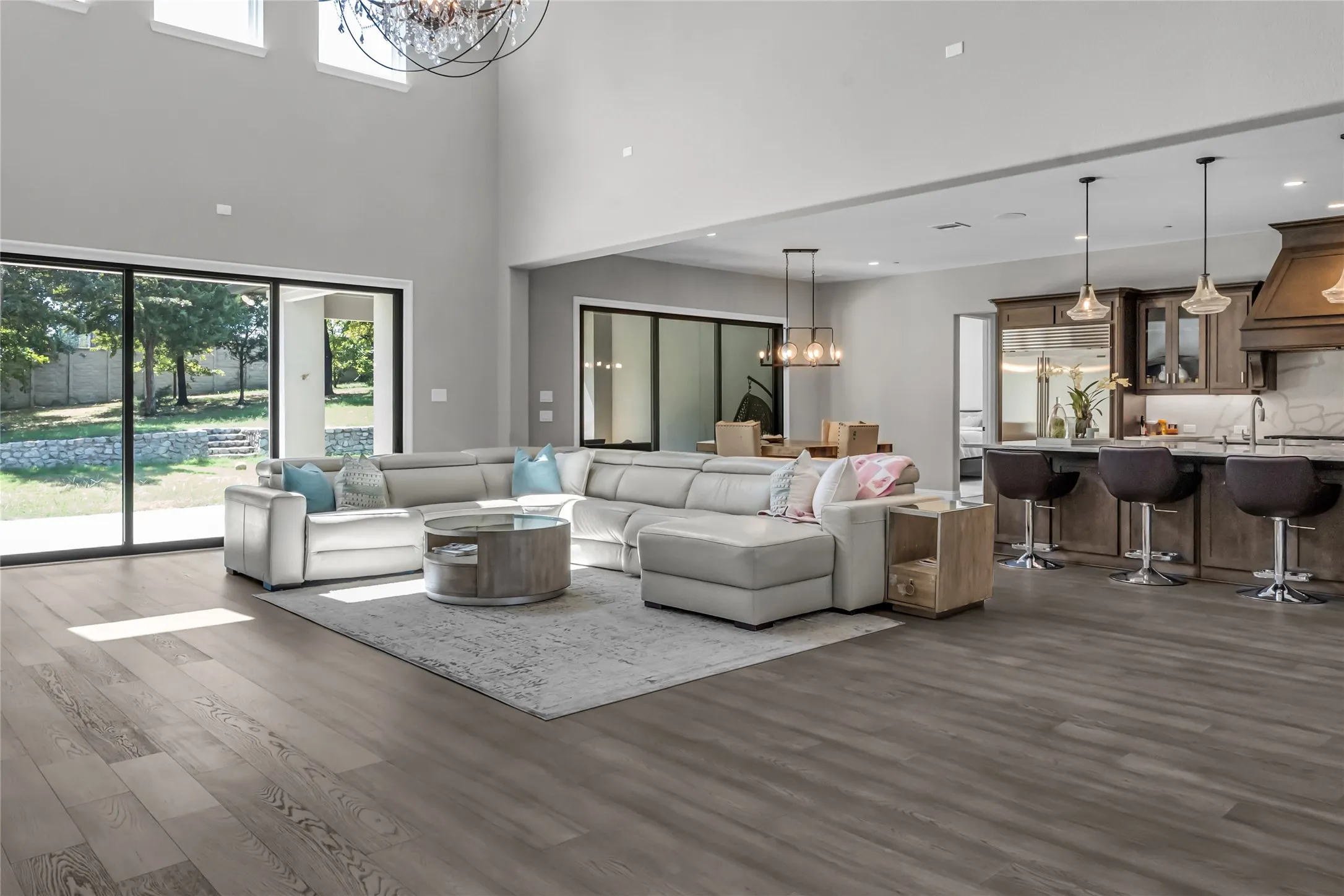 Vaulted ceilings with a statement chandelier, expansive wood-finish flooring, sliding glass doors to the backyard, a kitchen island with pendant lighting, and custom wood cabinetry