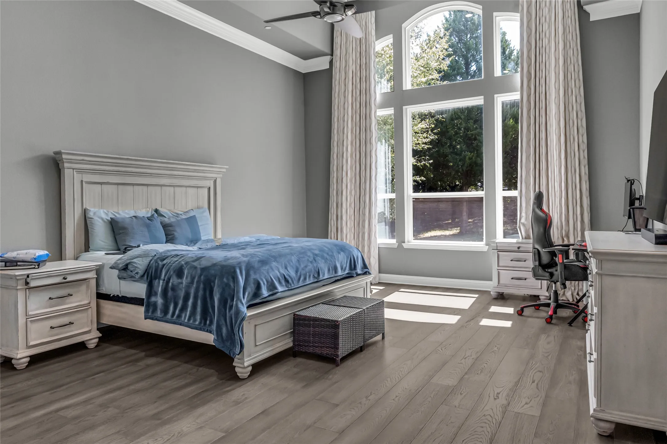 Arched window with multiple panes, wood-finish flooring, ceiling fan, crown molding, and high ceilings