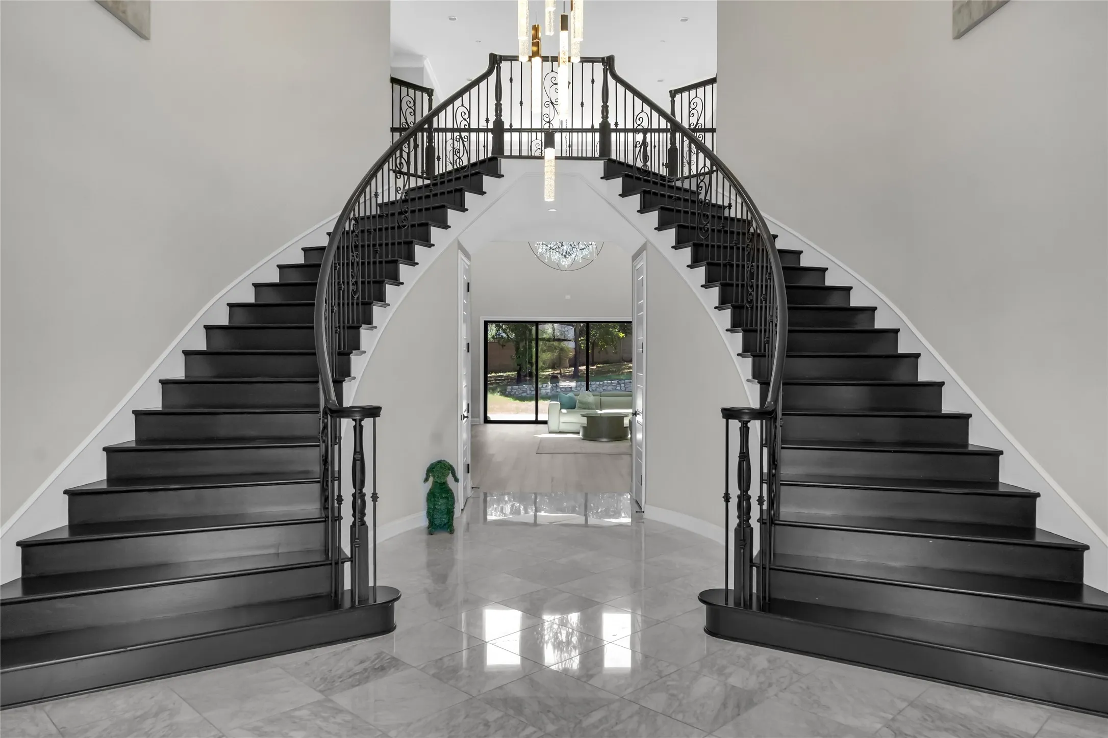 Grand double staircase with dark wood treads, ornate metal railings, and a polished tile floor