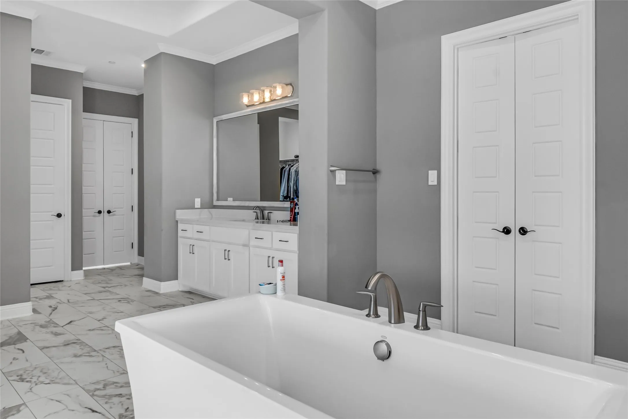 Freestanding soaking tub with brushed nickel fixtures, double vanity with white cabinetry, tile flooring, and white paneled doors