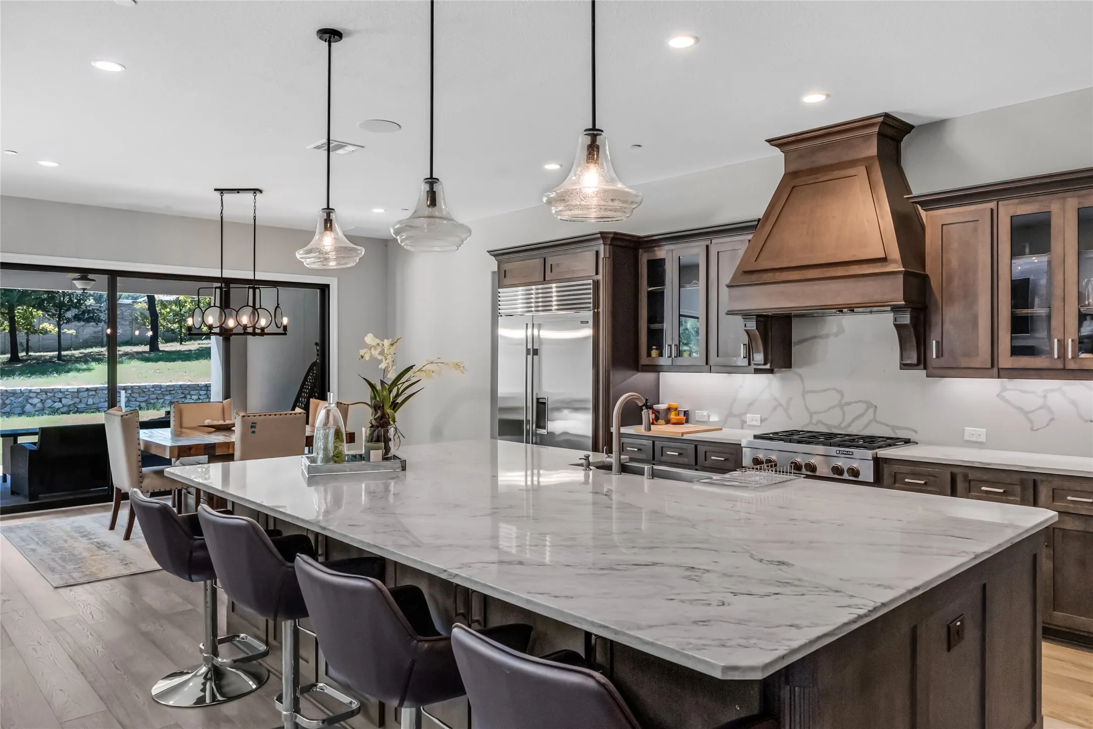 Spacious kitchen featuring a large island with stone countertop, wood-finish cabinetry, stainless steel appliances, and a decorative range hood