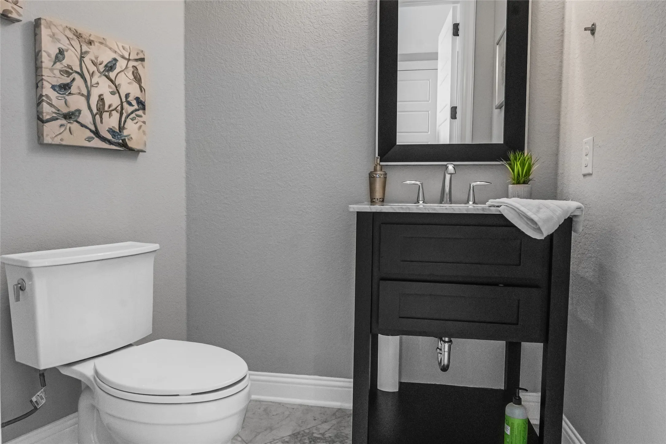 White toilet with a dark-finish vanity, polished chrome faucet, rectangular framed mirror, and light-toned flooring
