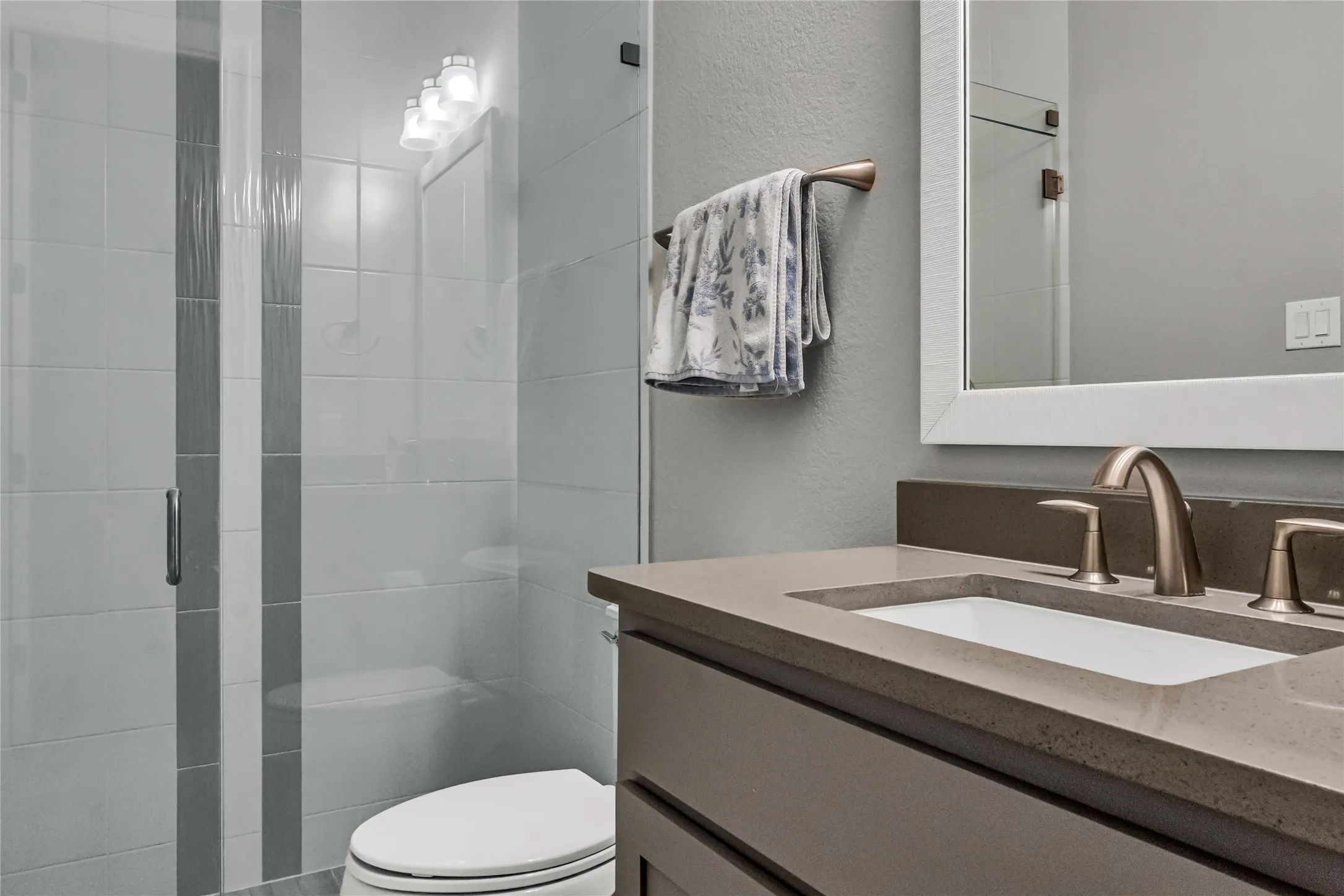 Glass-enclosed shower with contrasting tile accents, vanity with integrated sink, and brushed nickel fixtures