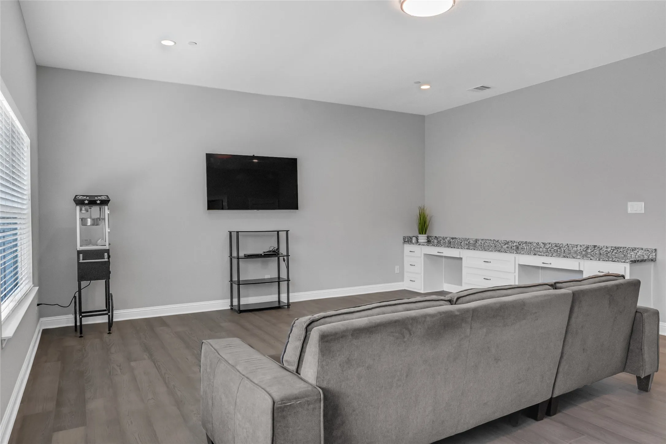 Spacious room featuring wood-finish flooring, recessed lighting, a large window, and built-in cabinetry with a stone countertop