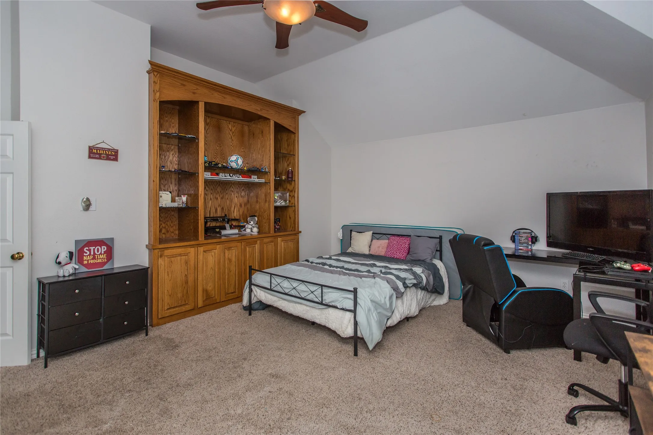 Built-in wood-finish cabinetry with glass shelving, vaulted ceiling, recessed door, and ceiling fan