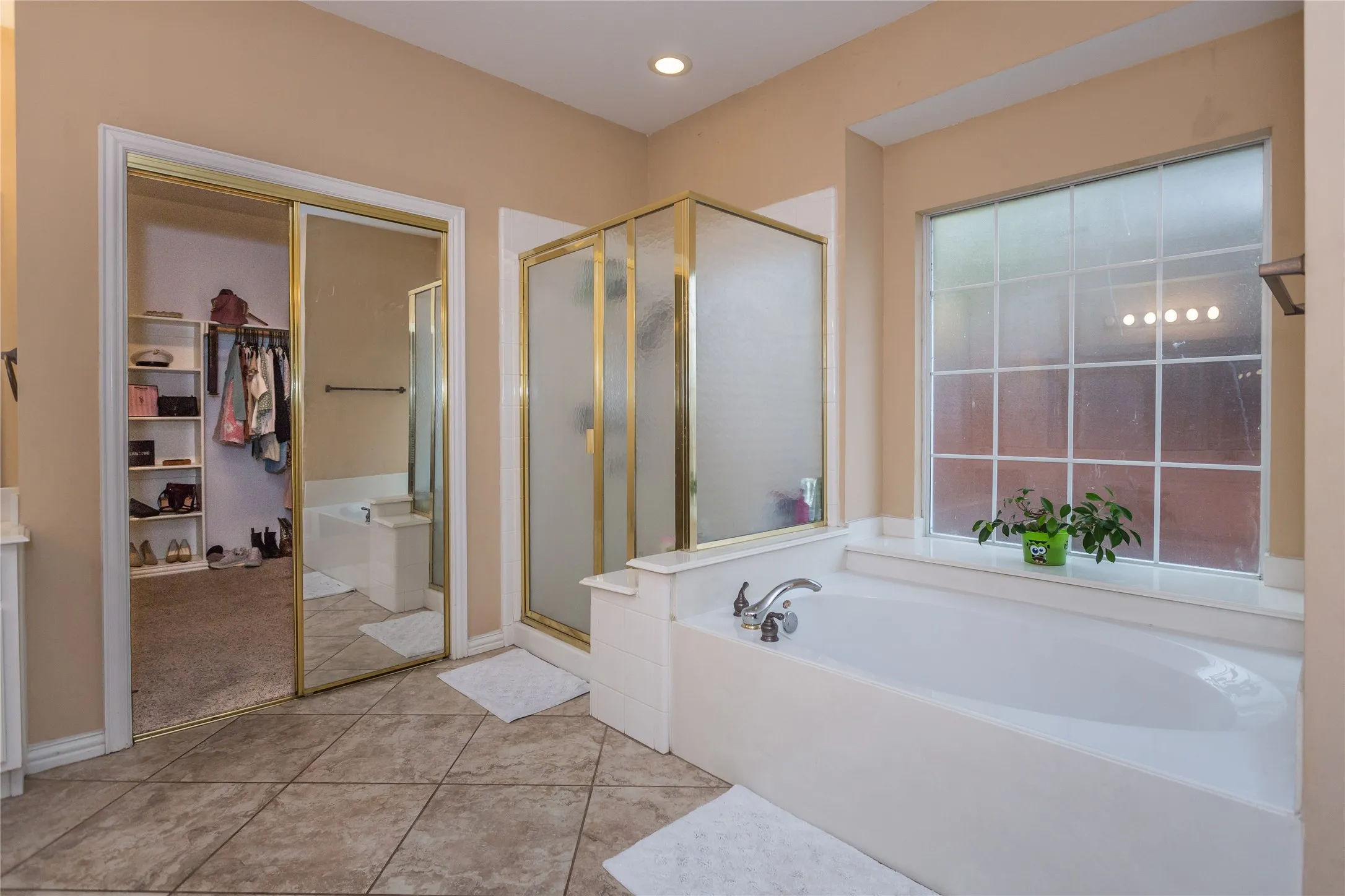 Ceramic tile flooring, built-in bathtub, glass-enclosed shower, large picture window with grid, and mirrored sliding closet doors