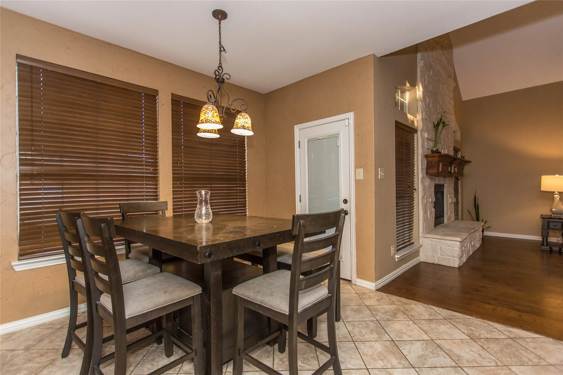 Stone fireplace with a wood mantle, vaulted ceilings, tile flooring, wood-finish flooring, and a glass-paneled door