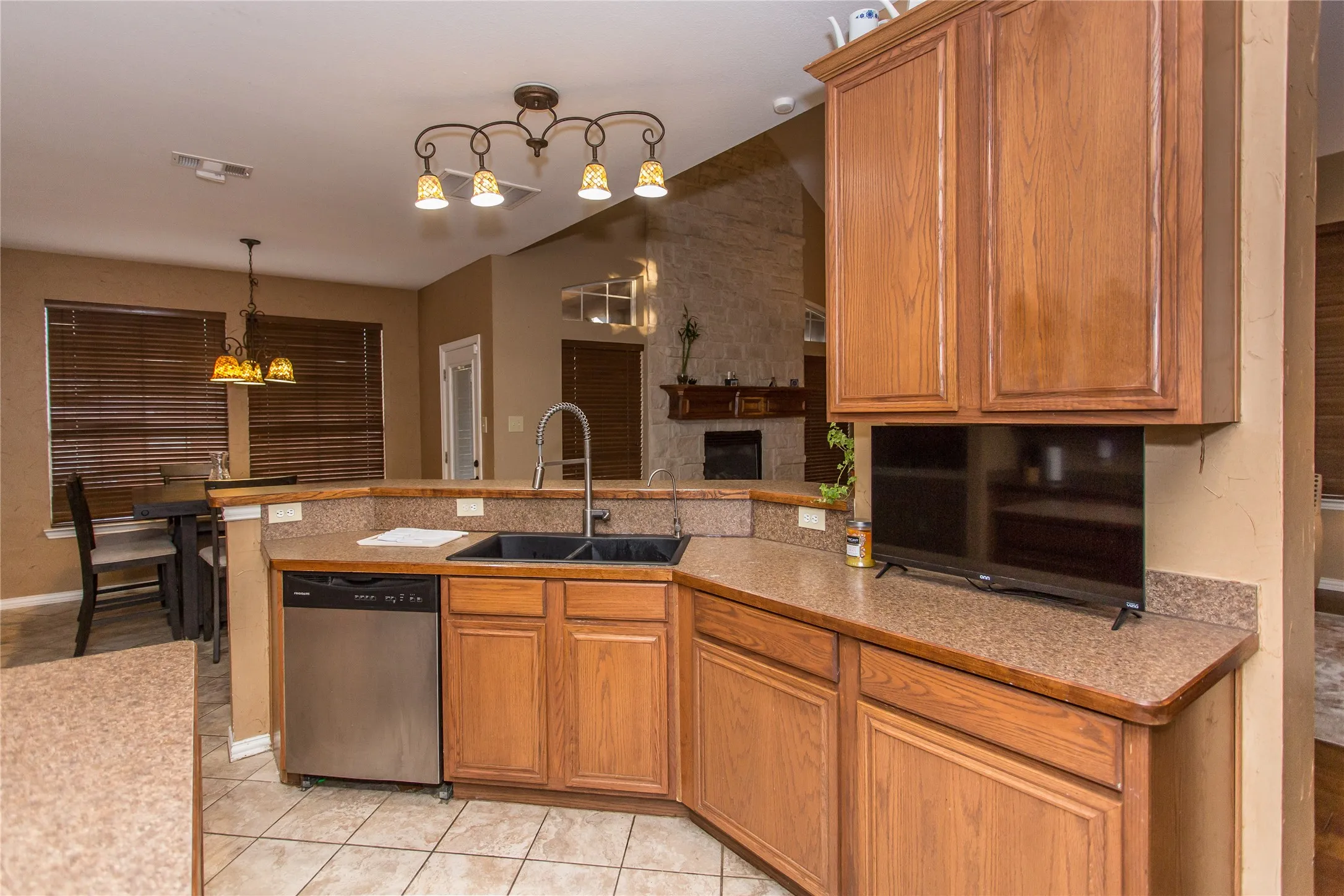 Kitchen featuring wood cabinetry, speckled countertops, stainless steel dishwasher, dual basin sink with gooseneck faucet, and tile flooring