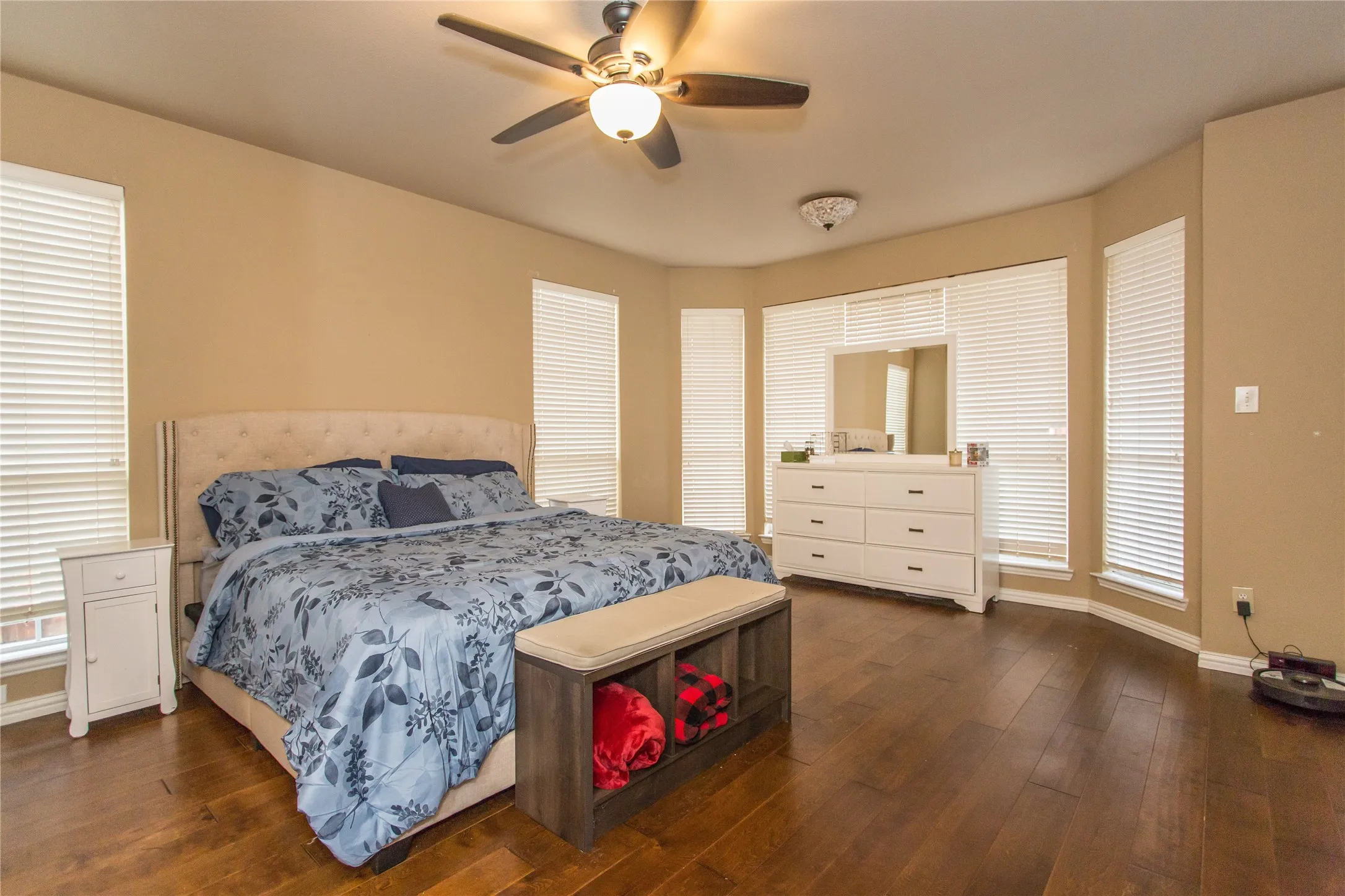 Wood-finish flooring, multiple windows with blinds, ceiling fan with integrated lighting, and a bay window area