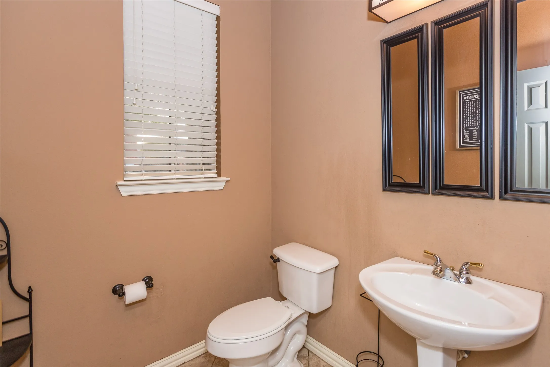 Pedestal sink with a two-handle faucet, white toilet, and window with horizontal blinds