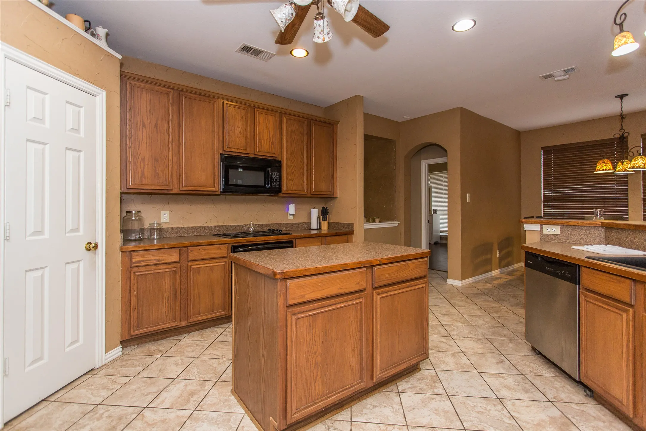 Kitchen featuring wood cabinetry, stone-finish countertops, stainless steel appliances, a central island, and tile flooring