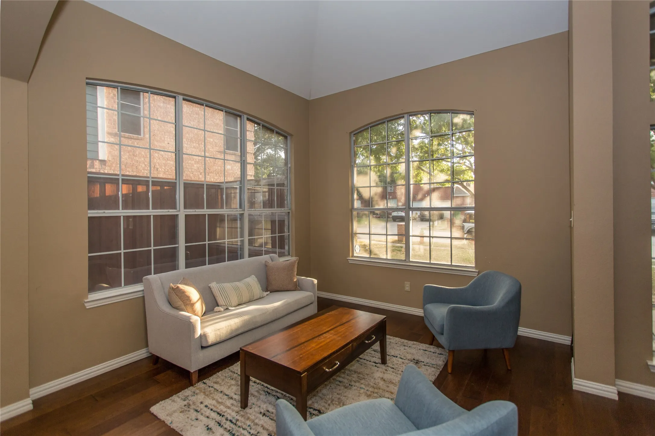 Vaulted ceiling, arched windows, dark wood-finish flooring, white trim, and neutral wall tones