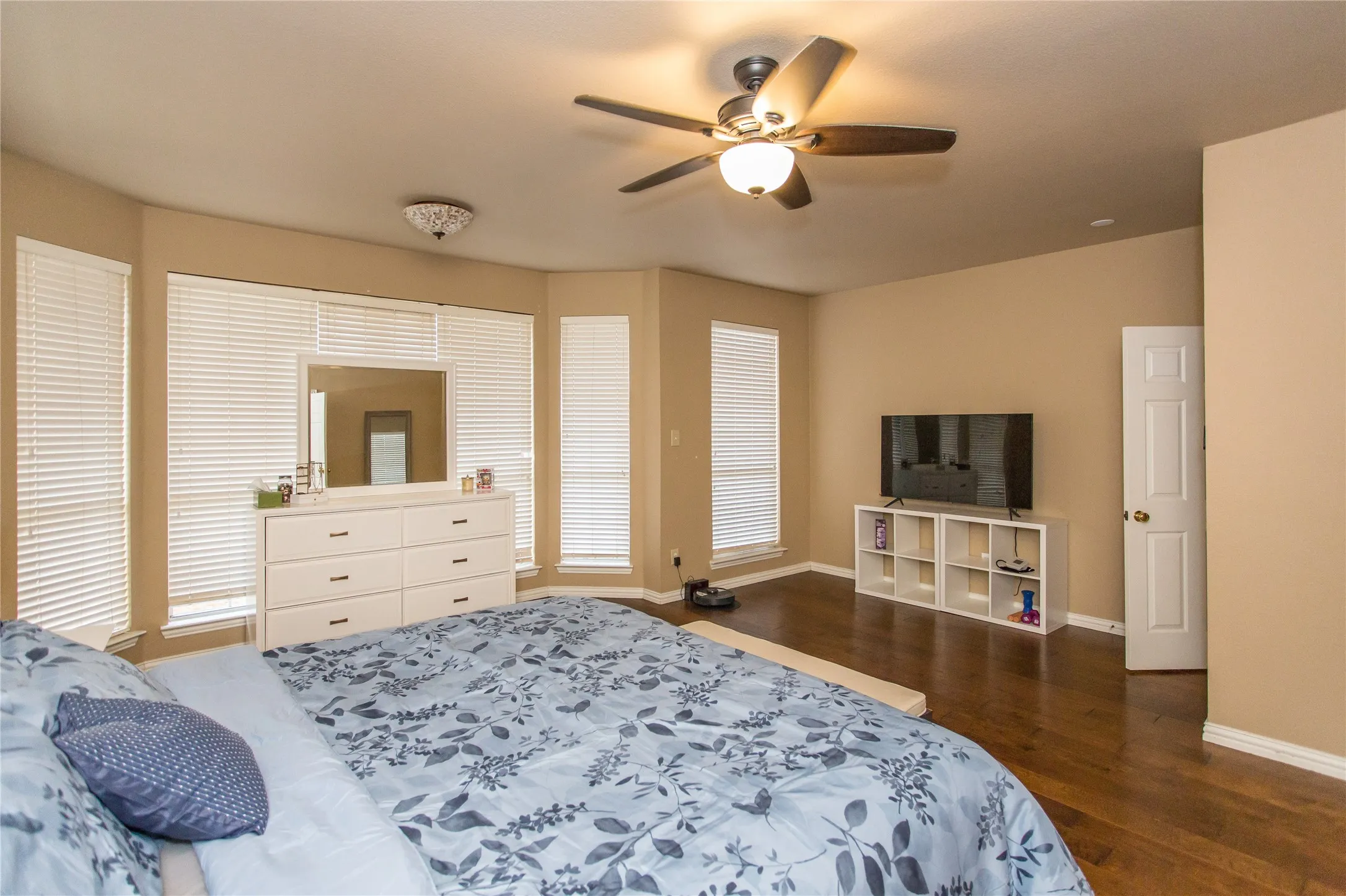 Wood-finish flooring, ceiling fan with integrated lighting, multiple windows with blinds, and neutral wall paint