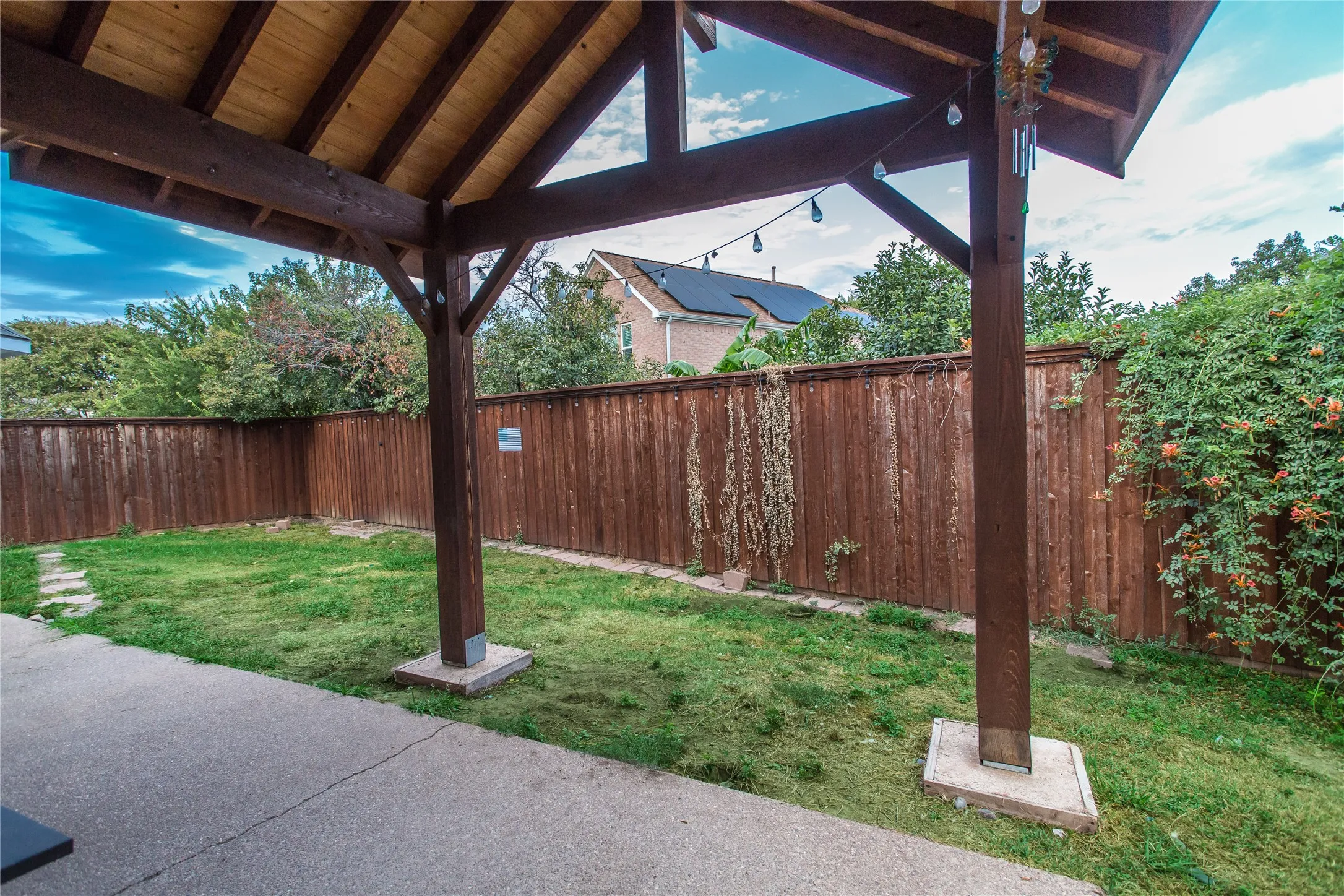 Covered outdoor patio with exposed wood beams, concrete slab, wood privacy fencing, and green lawn