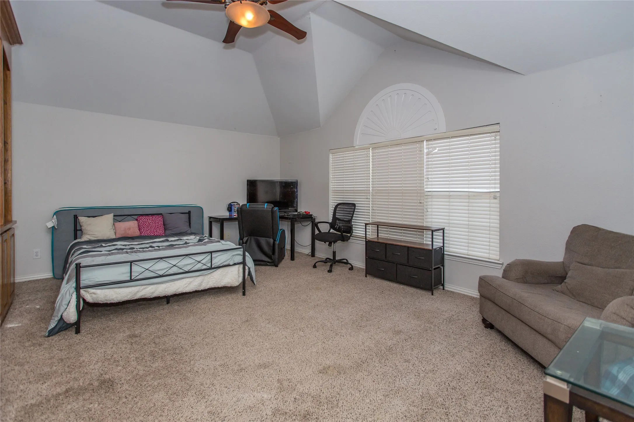 Vaulted ceiling with ceiling fan, large window with blinds, decorative arched transom window, and neutral carpet flooring
