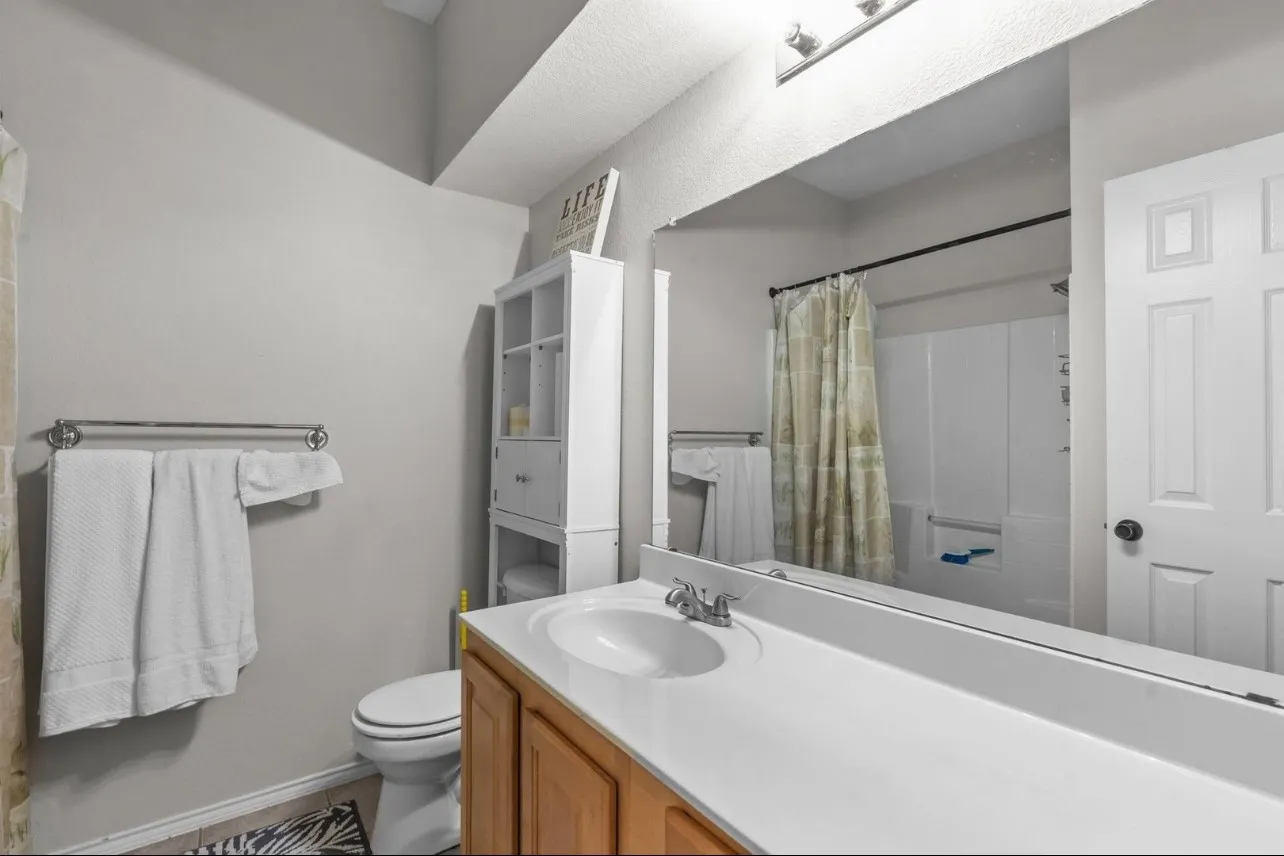 Bathroom featuring a single vanity, wood-finish cabinetry, a large wall-mounted mirror, and a shower-tub combination